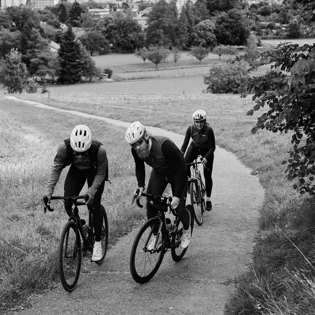 Three cyclists in aero position on time trial bikes riding through park landscape in black and white