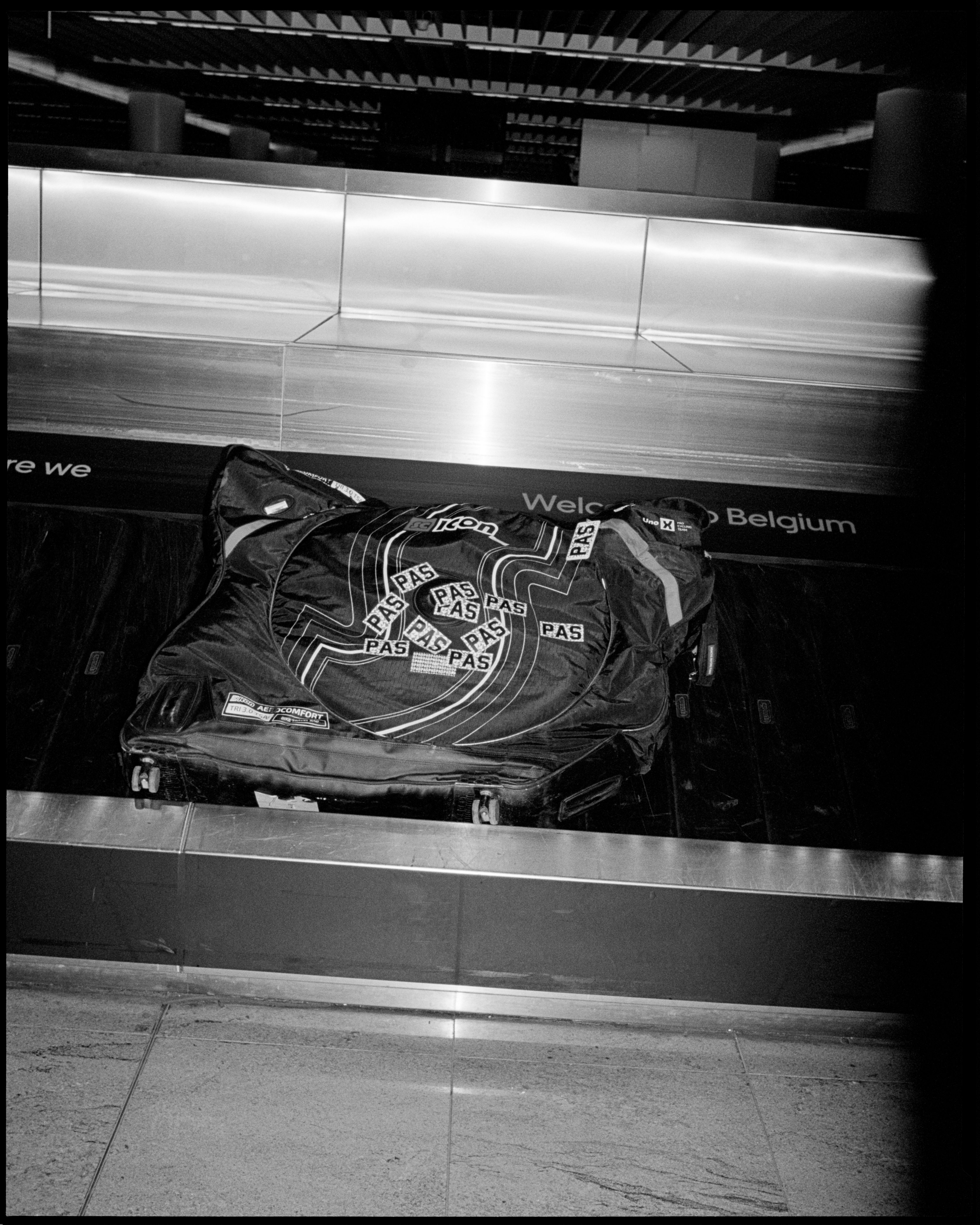 Black cycling bag with geometric pattern and logo branding on airport luggage conveyor belt