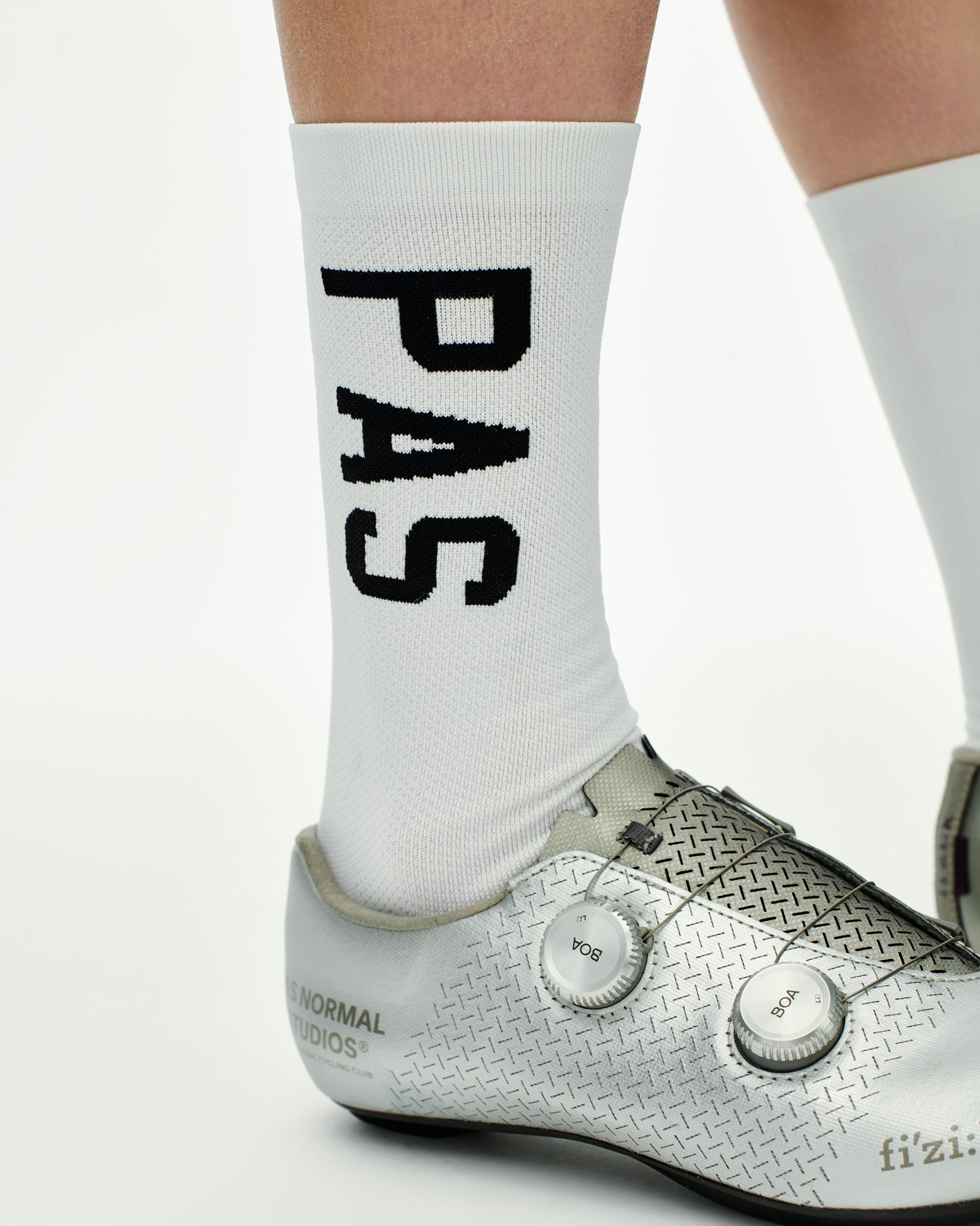 White PAS cycling socks on model with black logo lettering and white road shoes with dual BOA dials