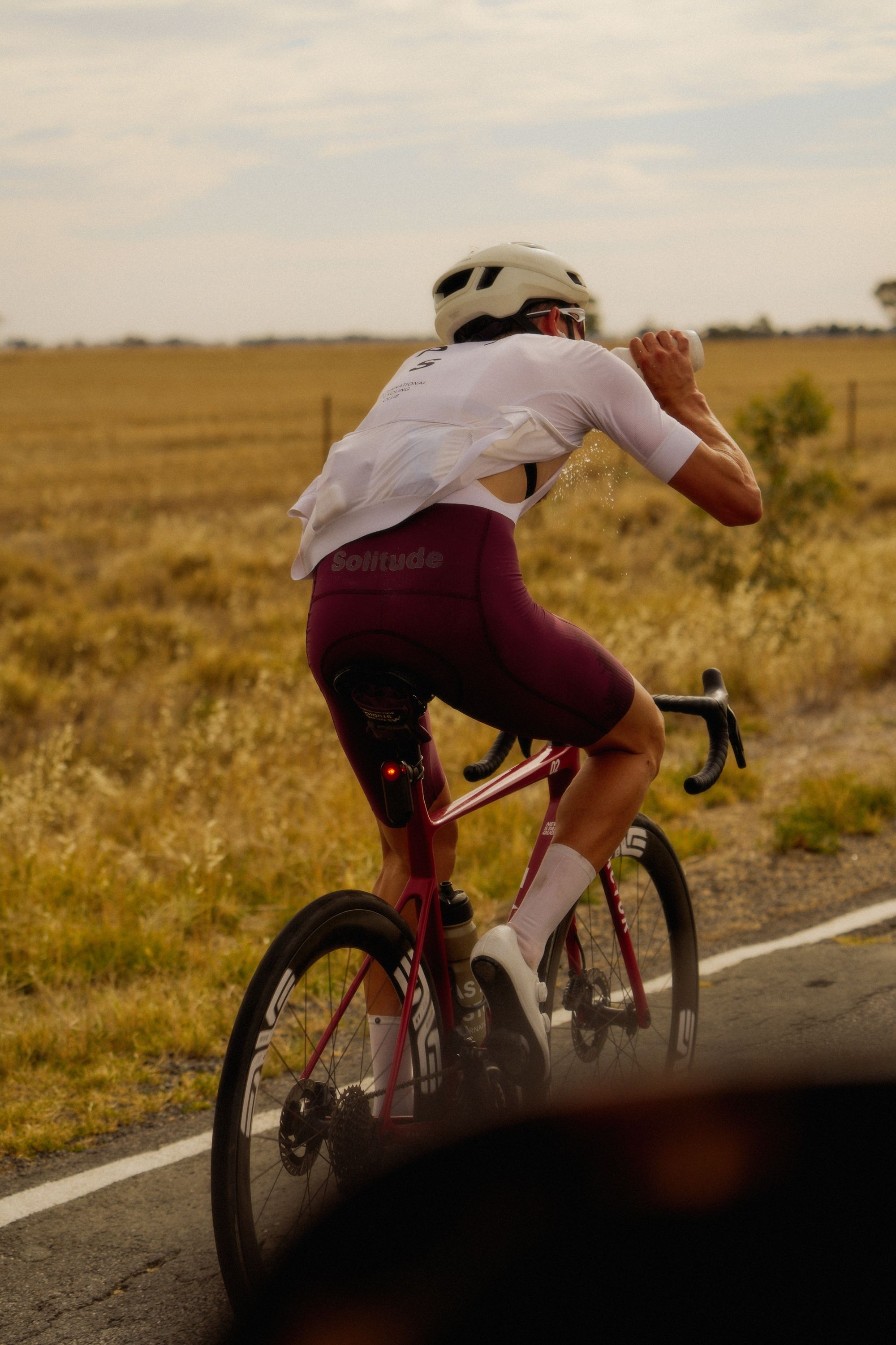 Model wearing white jersey and burgundy shorts cycling on time trial bike on countryside road