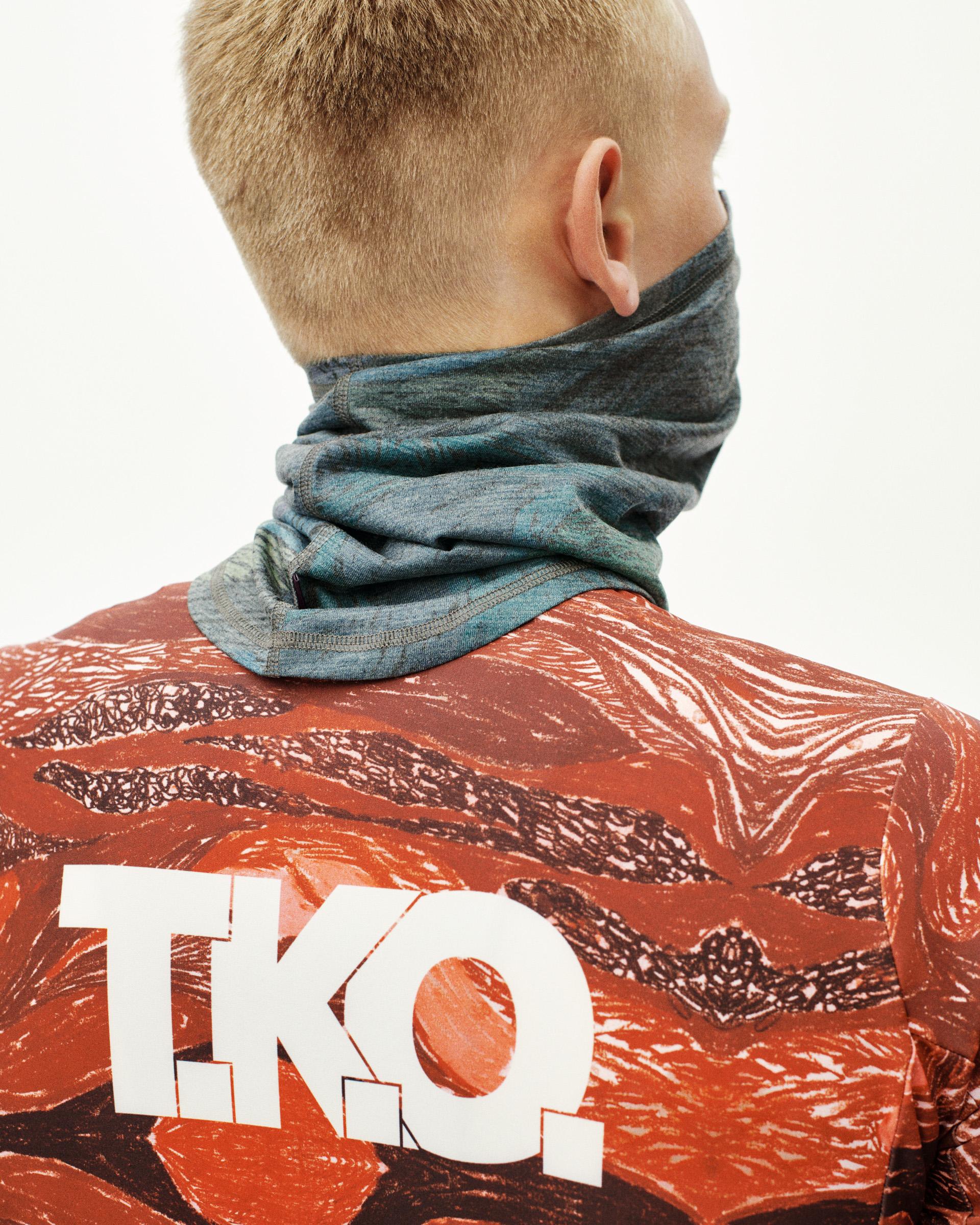 Dark Multi T.K.O. Merino necktube on model, rear view with blue-grey marl texture and abstract red print jersey behind