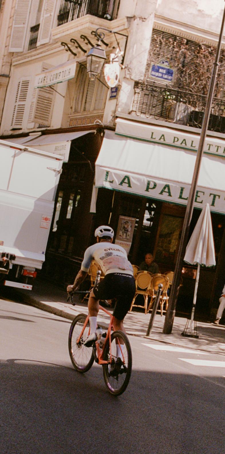 Cyclist in white kit riding past French cafe on city street