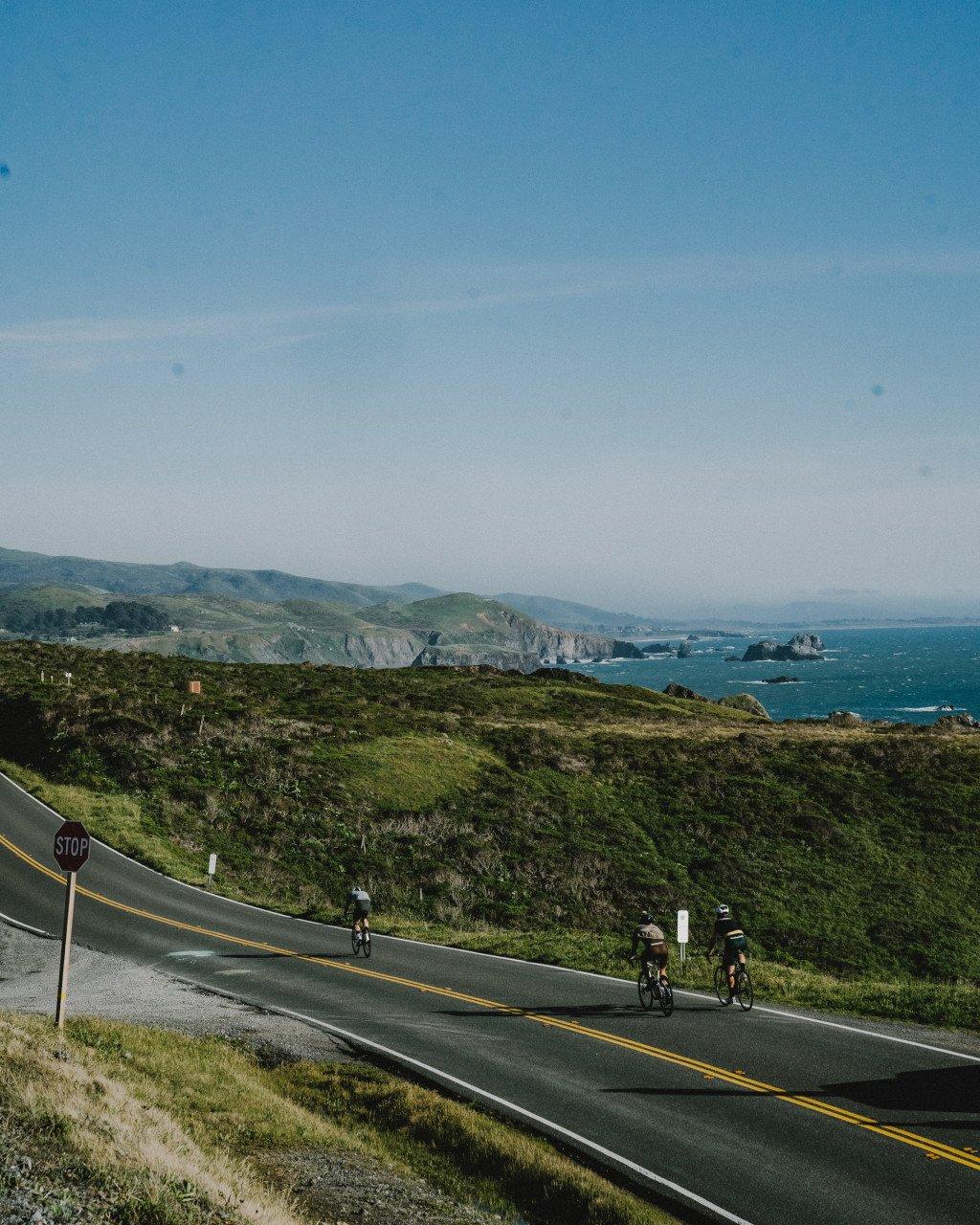 Cyclists riding along coastal highway with ocean and cliffs in background