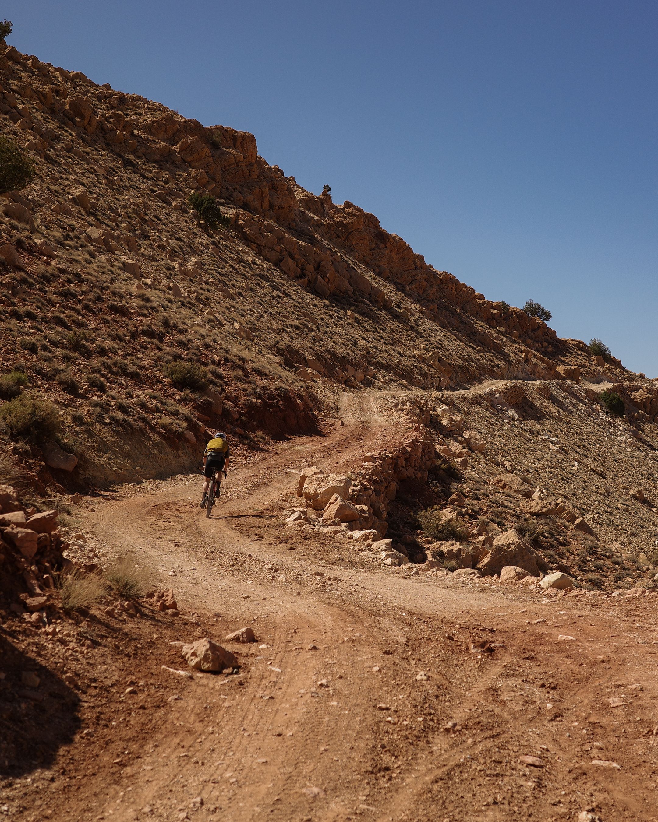 Cyclist in yellow jersey riding gravel bike on desert dirt road through rocky canyon landscape
