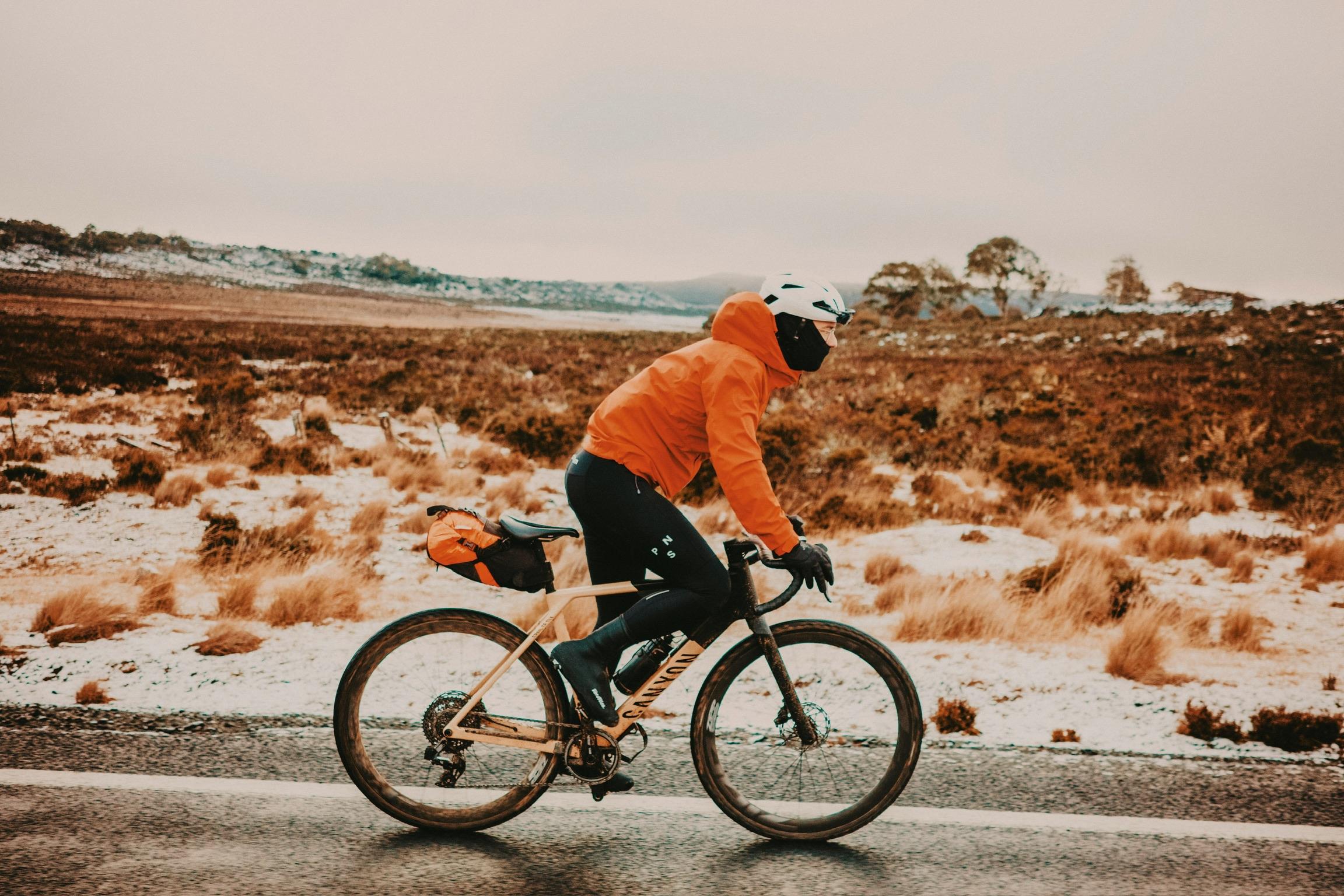 Cyclist in orange jacket riding through snowy Tasmanian landscape on gravel road