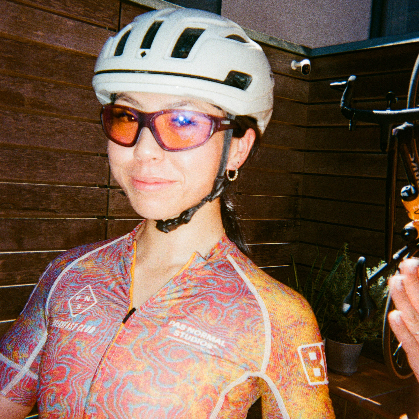 Model wearing colorful patterned cycling jersey with white helmet and sunglasses