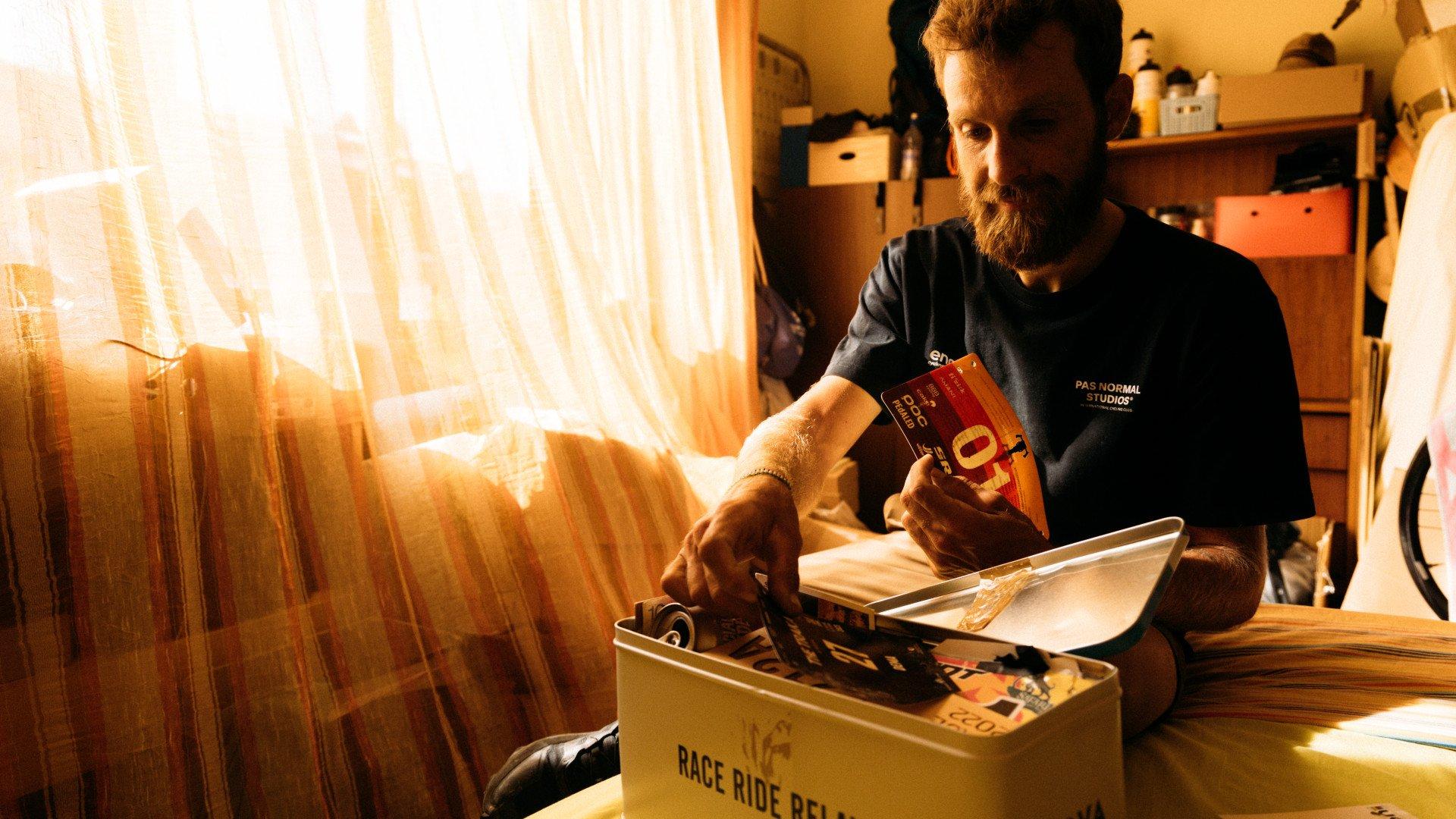 Model wearing dark blue t-shirt with chest branding browsing cycling magazines in warm indoor setting