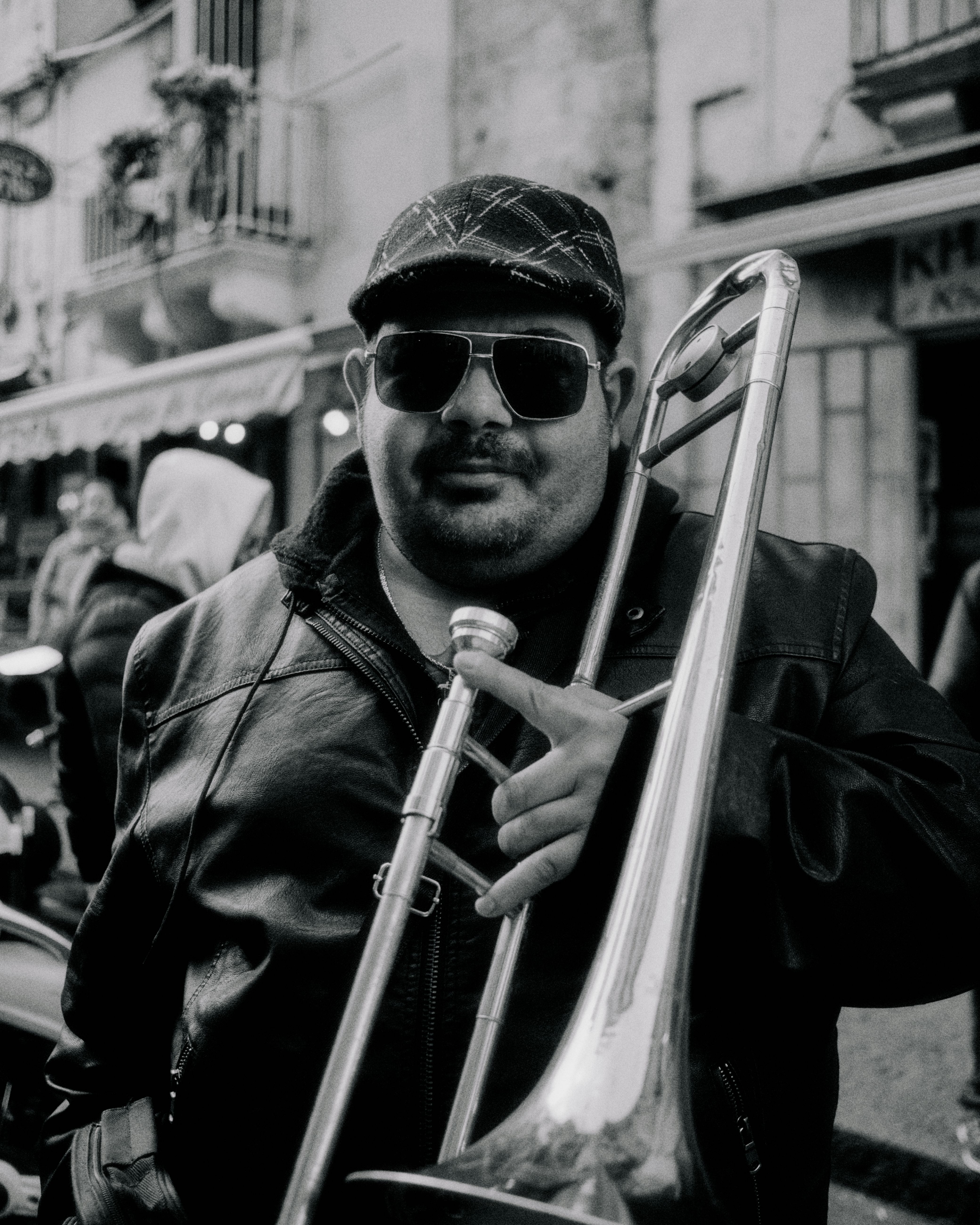 Model wearing patterned cycling cap with sunglasses holding trombone on Sicily street