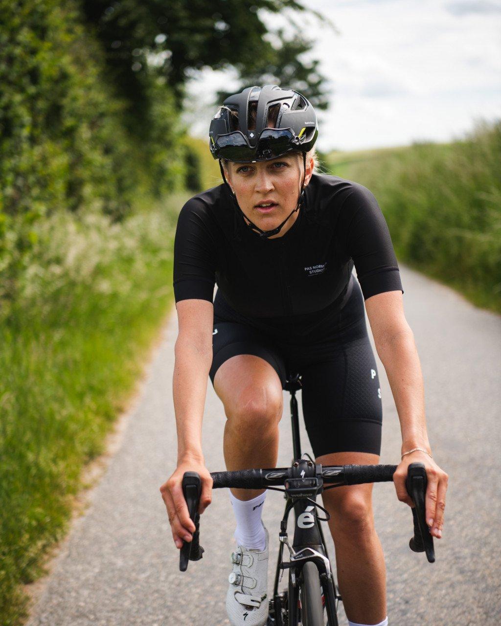 Model wearing black cycling skinsuit with chest branding on time trial bike on country road