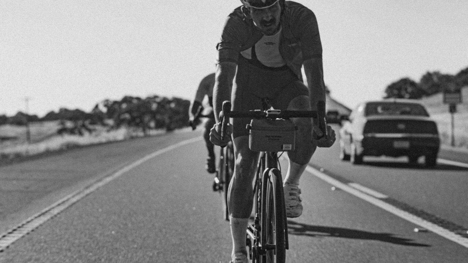 Cyclist on road bike in aerodynamic position on rural road, black and white photography