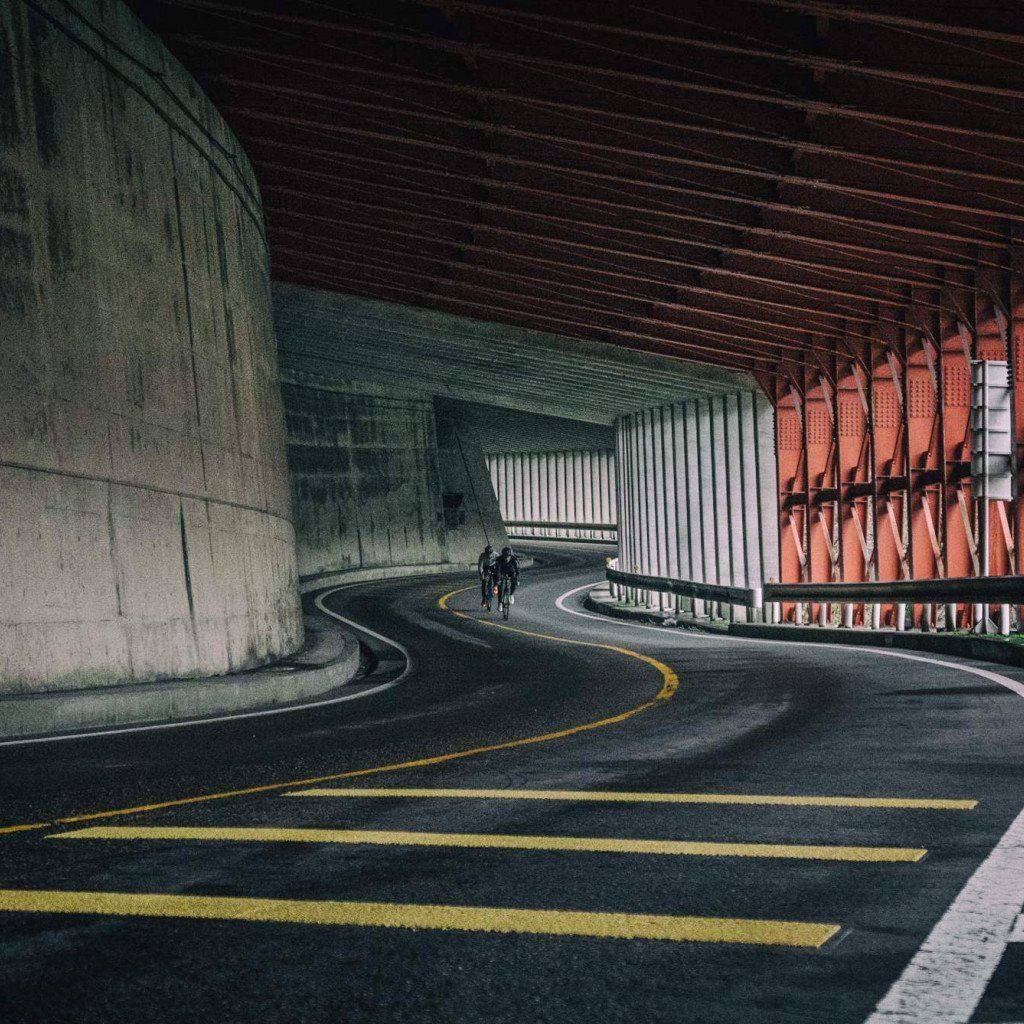 Cyclists riding through curved concrete tunnel with orange architectural details in Toyama, Japan