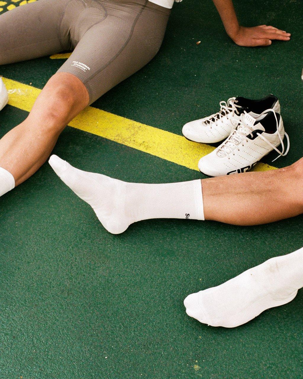 White cycling socks with small logo detail, worn with grey shorts on tennis court surface