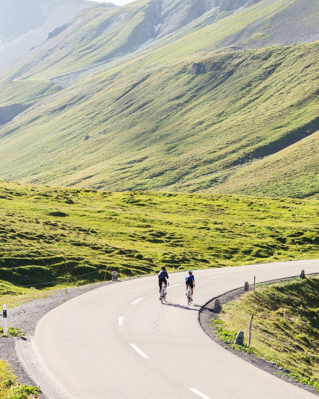 Two cyclists riding on mountain road through green hills and valleys