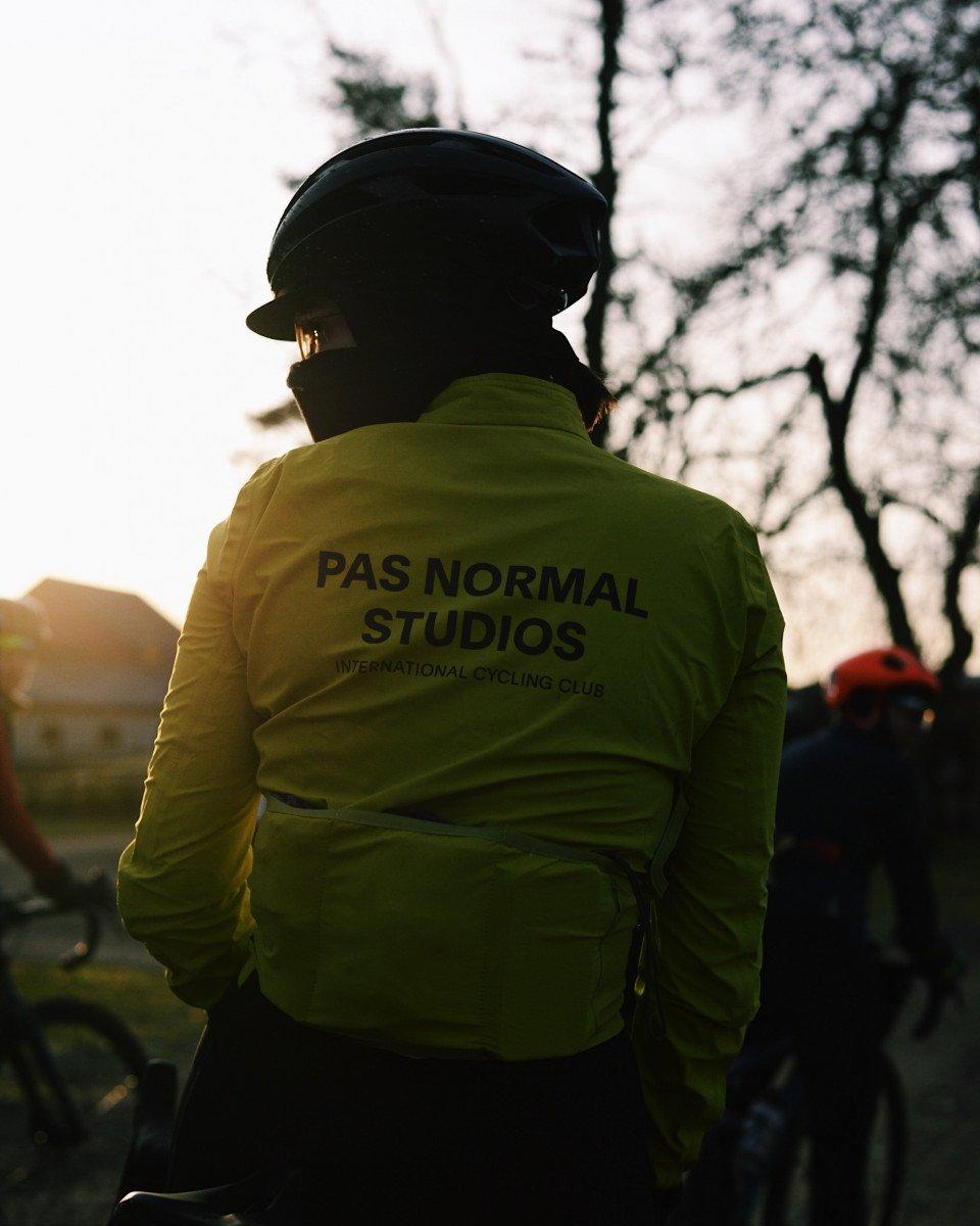Model wearing green cycling jacket with back branding, silhouetted against trees at sunset