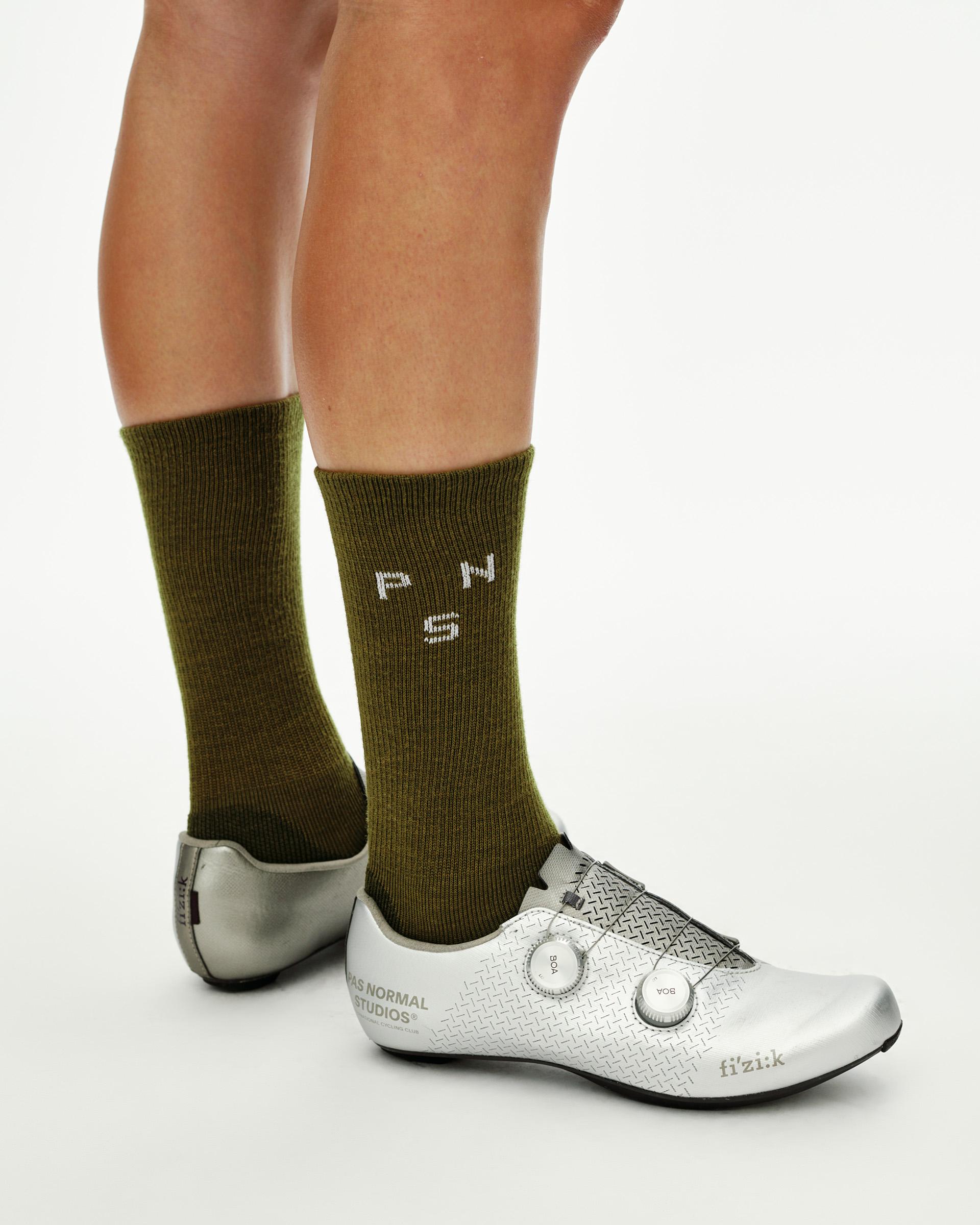 Khaki Green Deep Winter Wool cycling socks on model, side view with white PNS logo knit into cuff