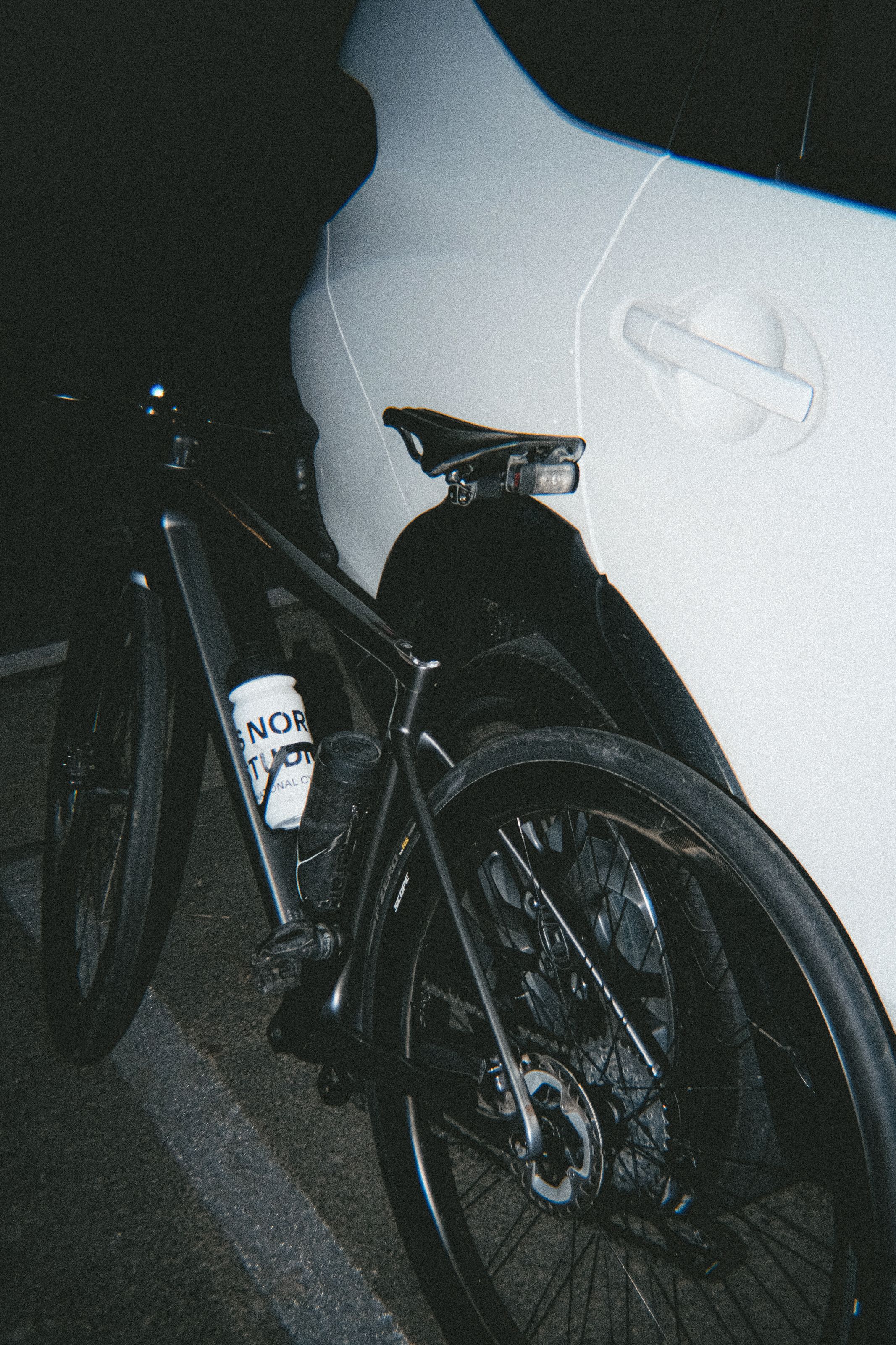 Black bicycle with water bottle in frame against white wall in dim lighting