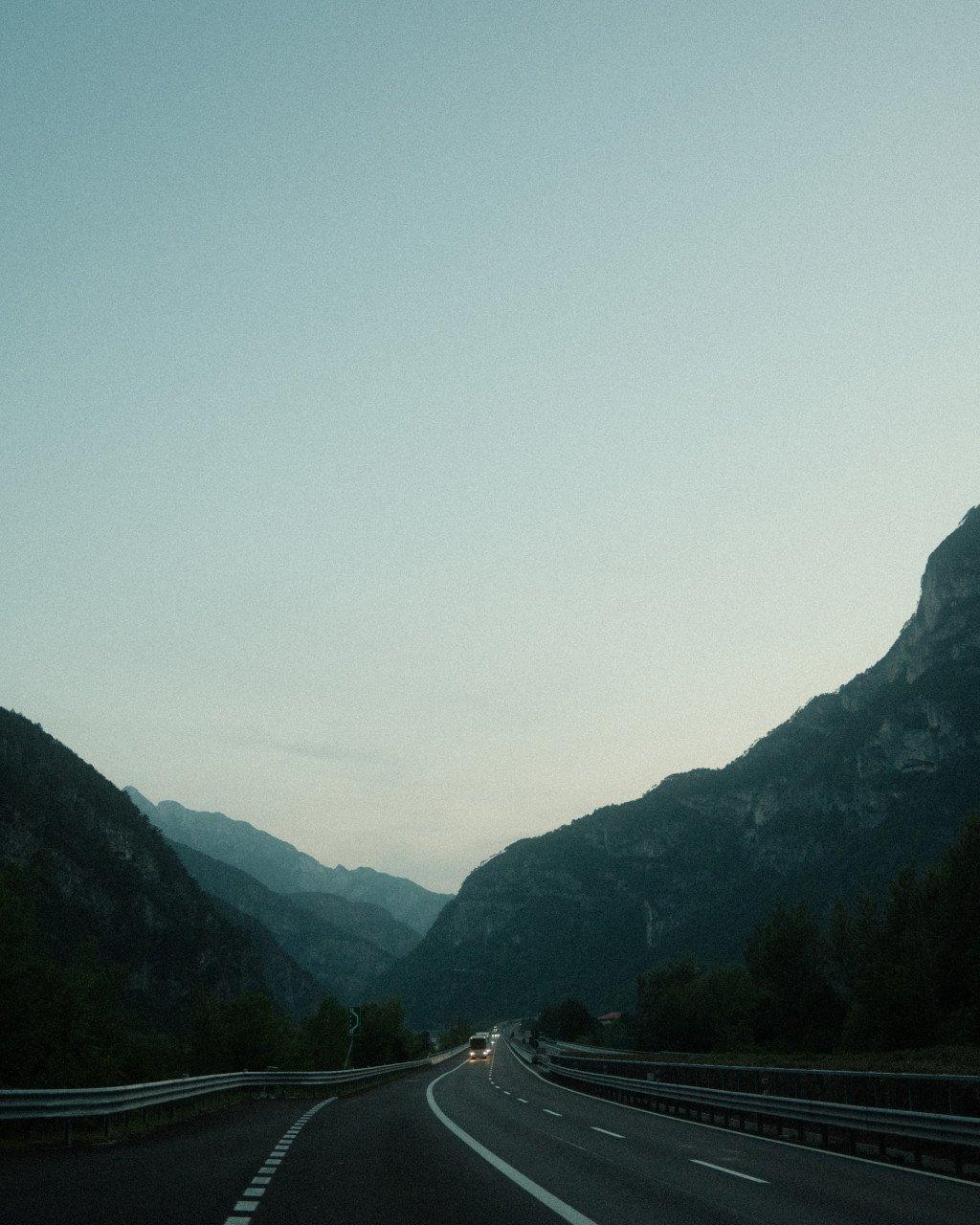 Mountain road winding through Slovenian valley at dusk with distant vehicle headlights