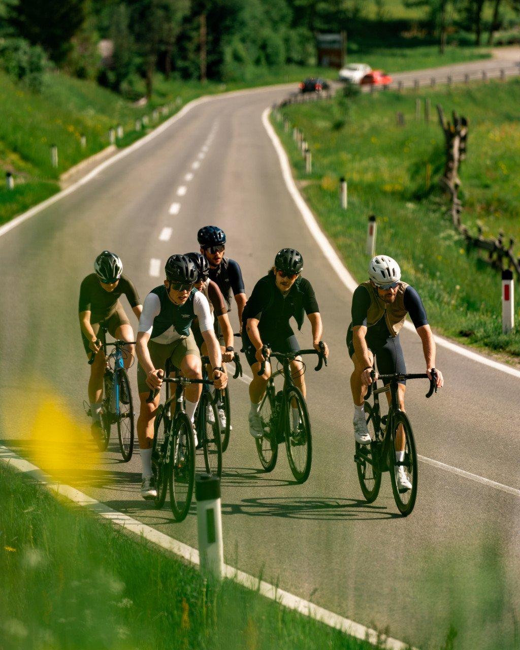 Group of cyclists in dark jerseys riding in formation on countryside road