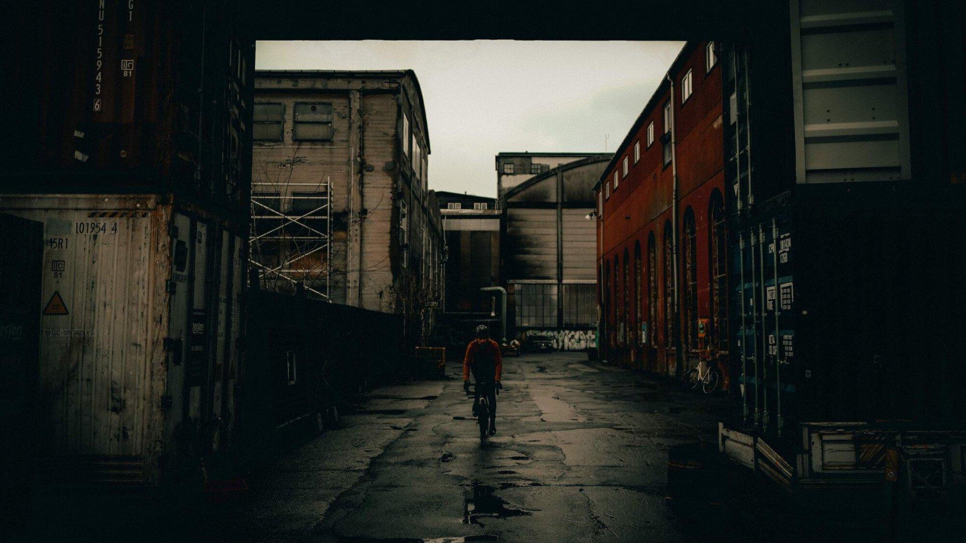 Cyclist riding through industrial urban alleyway between weathered brick buildings