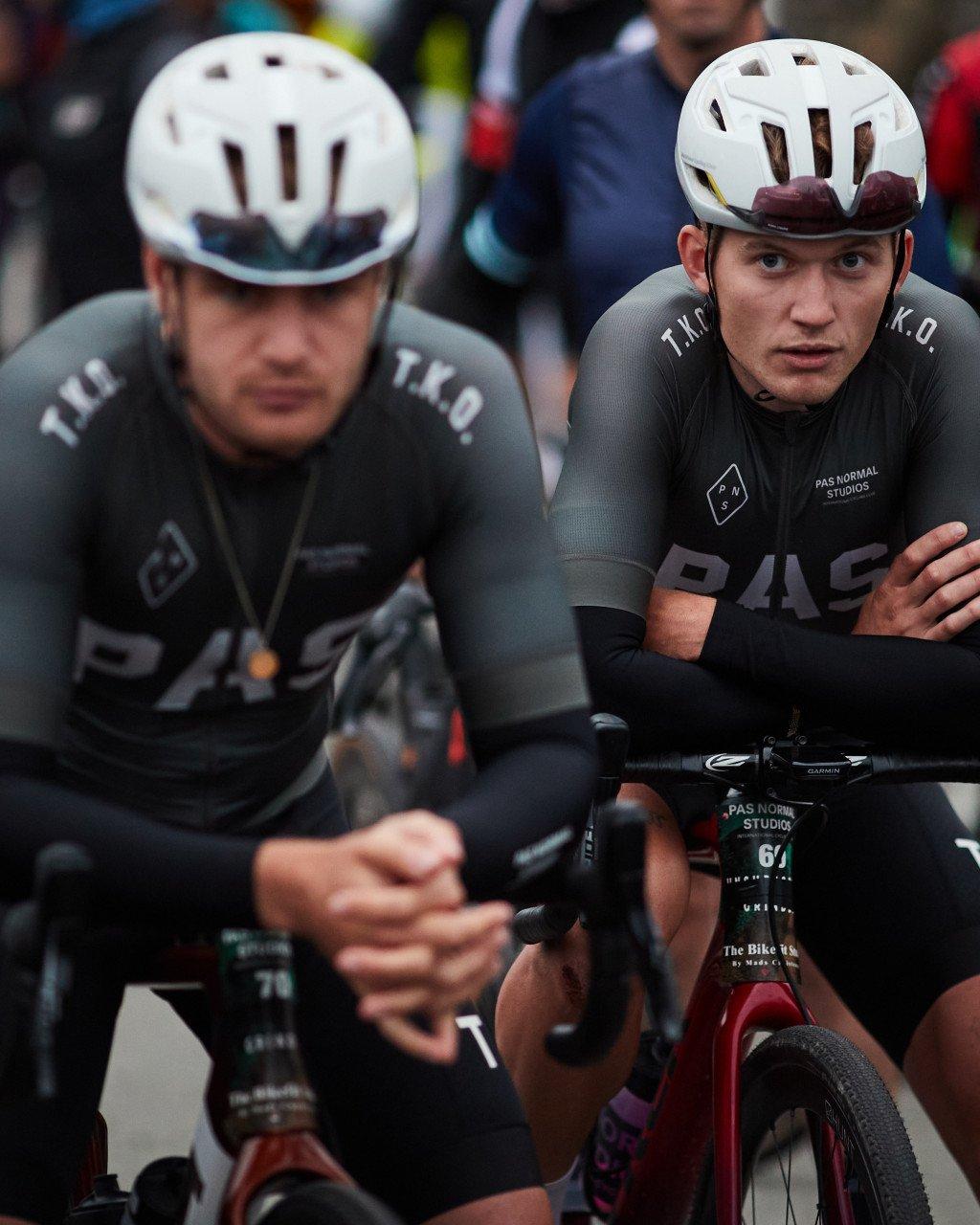 Two cyclists in black time trial suits with white helmets preparing for race start
