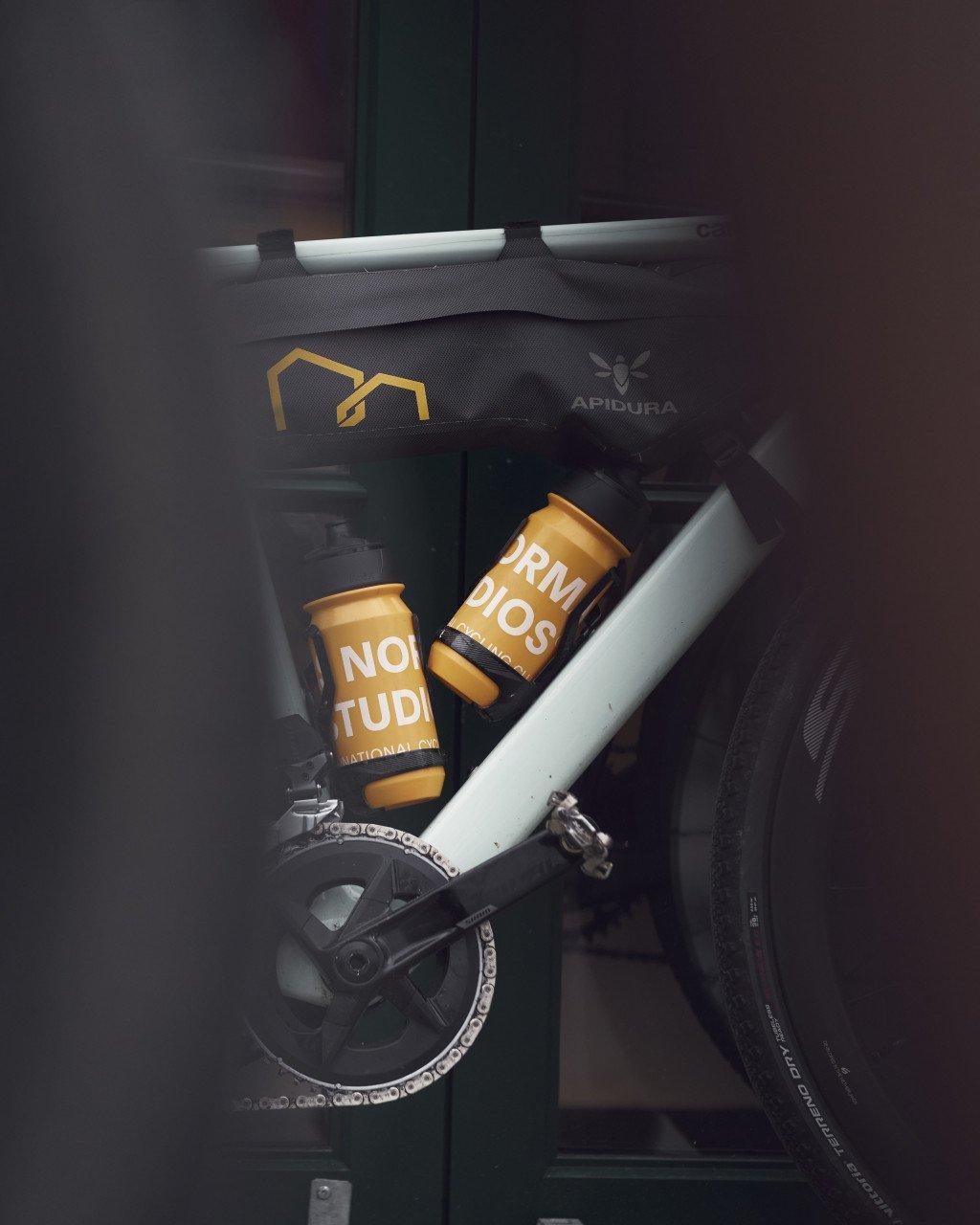 Dark frame bag with yellow logo mounted on white bicycle frame with two orange bidons