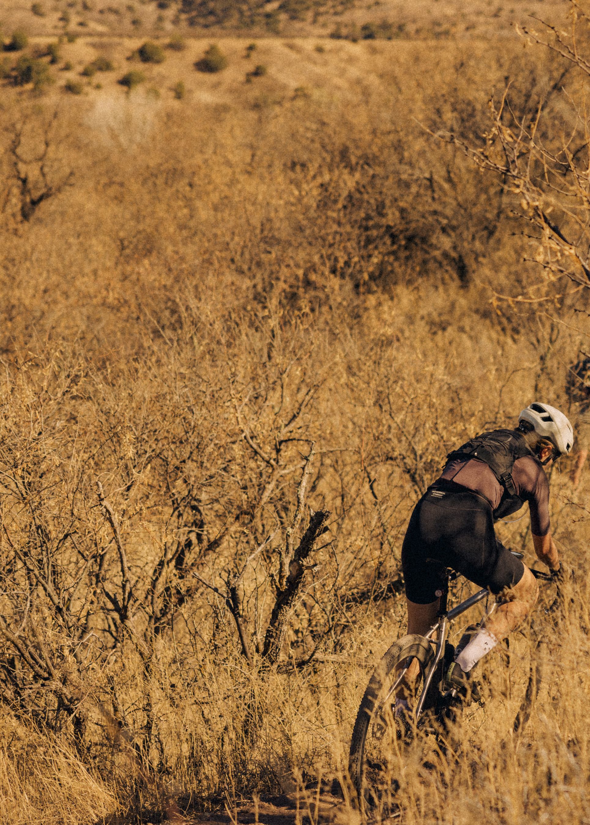 Model wearing black cycling jersey and shorts mountain biking through desert terrain in golden light