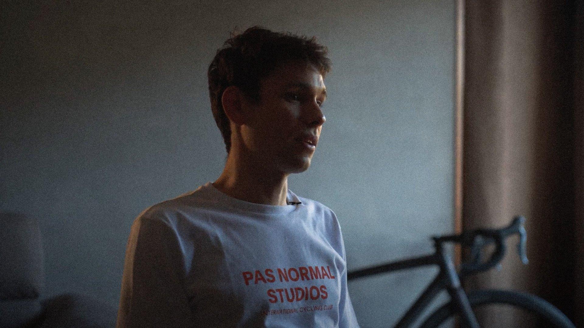 Model wearing white t-shirt with red chest lettering in indoor setting with bicycle in background