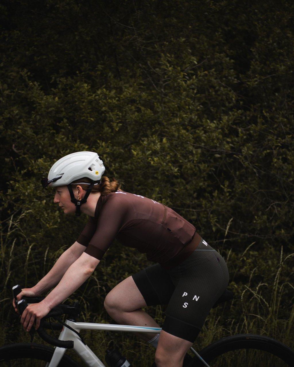 Model wearing brown cycling jersey and black shorts in aerodynamic position on time trial bike