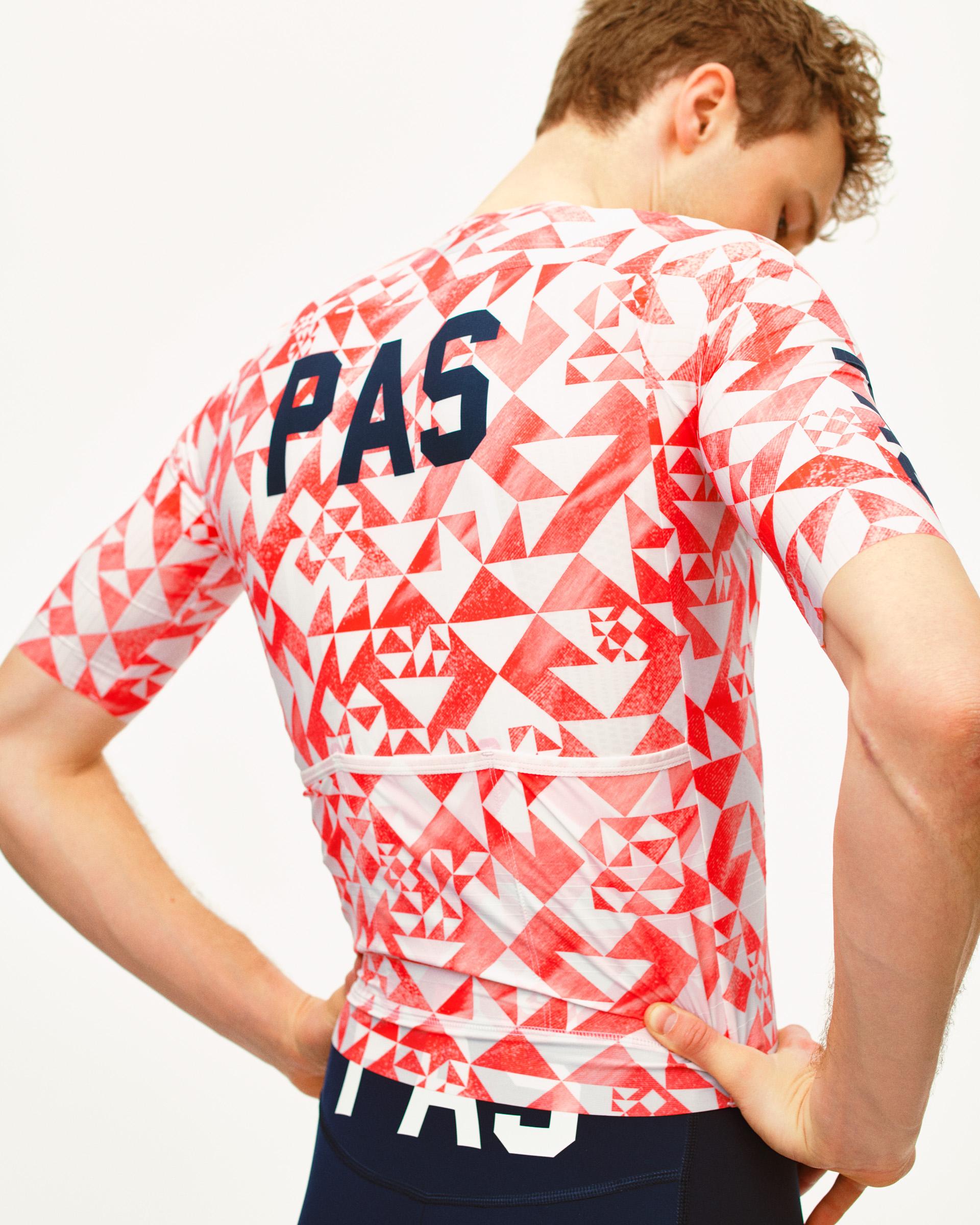 White PAS Mechanism Pro cycling jersey on model, rear view with red geometric origami print