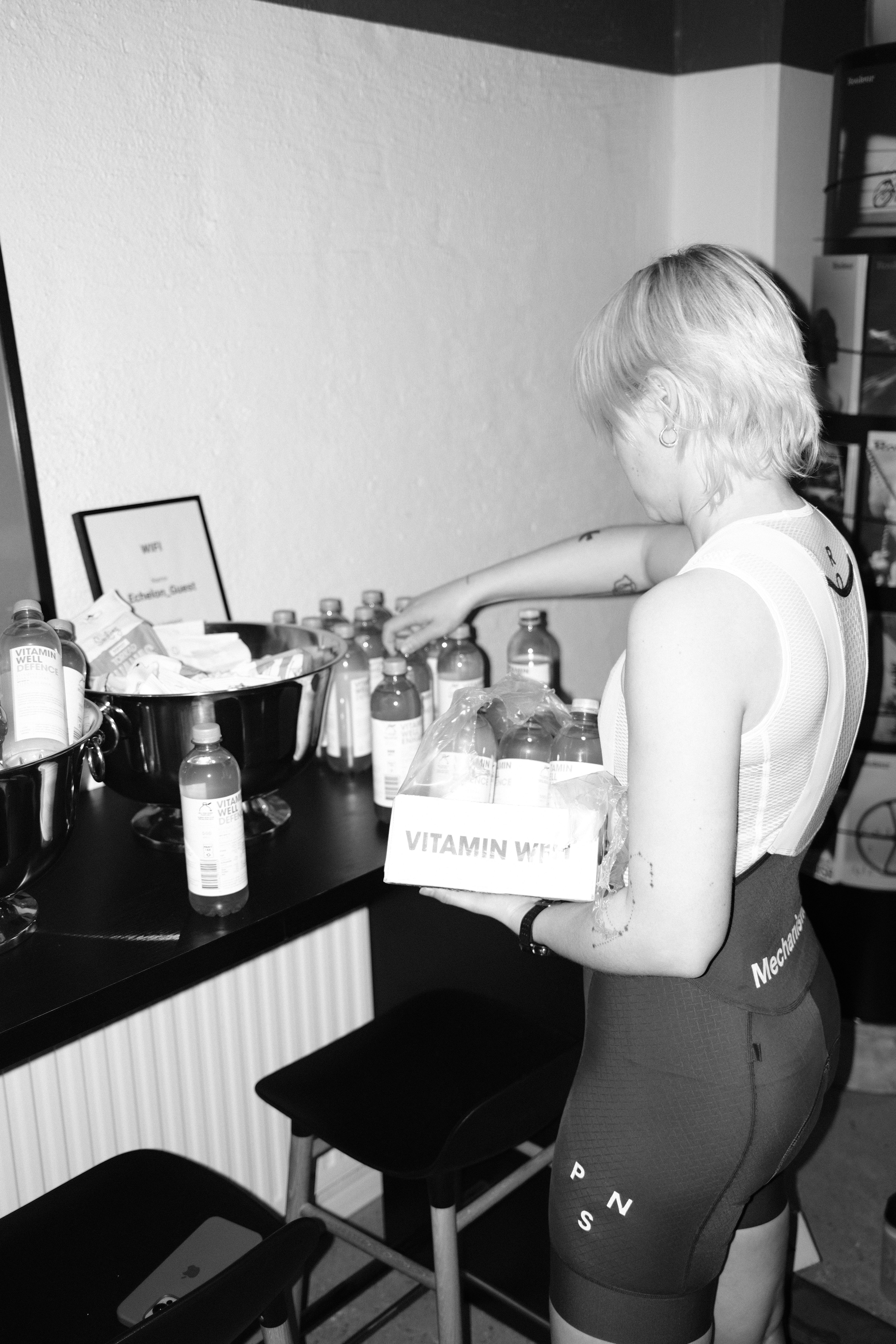 Model wearing Mechanism sleeveless jersey and bib shorts at kitchen counter with vitamin supplements