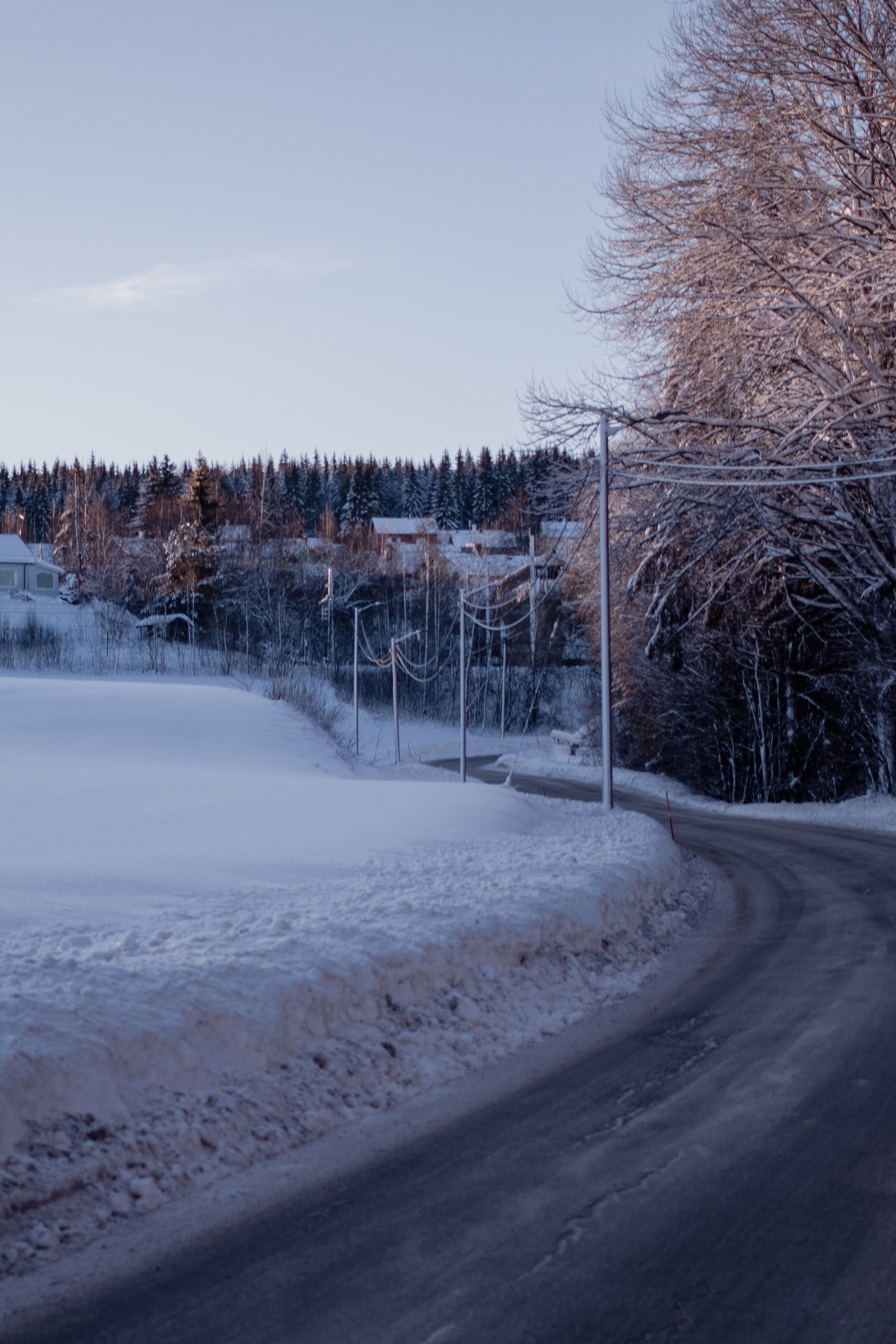 Snow-covered road winding through winter landscape with frost-laden trees and houses