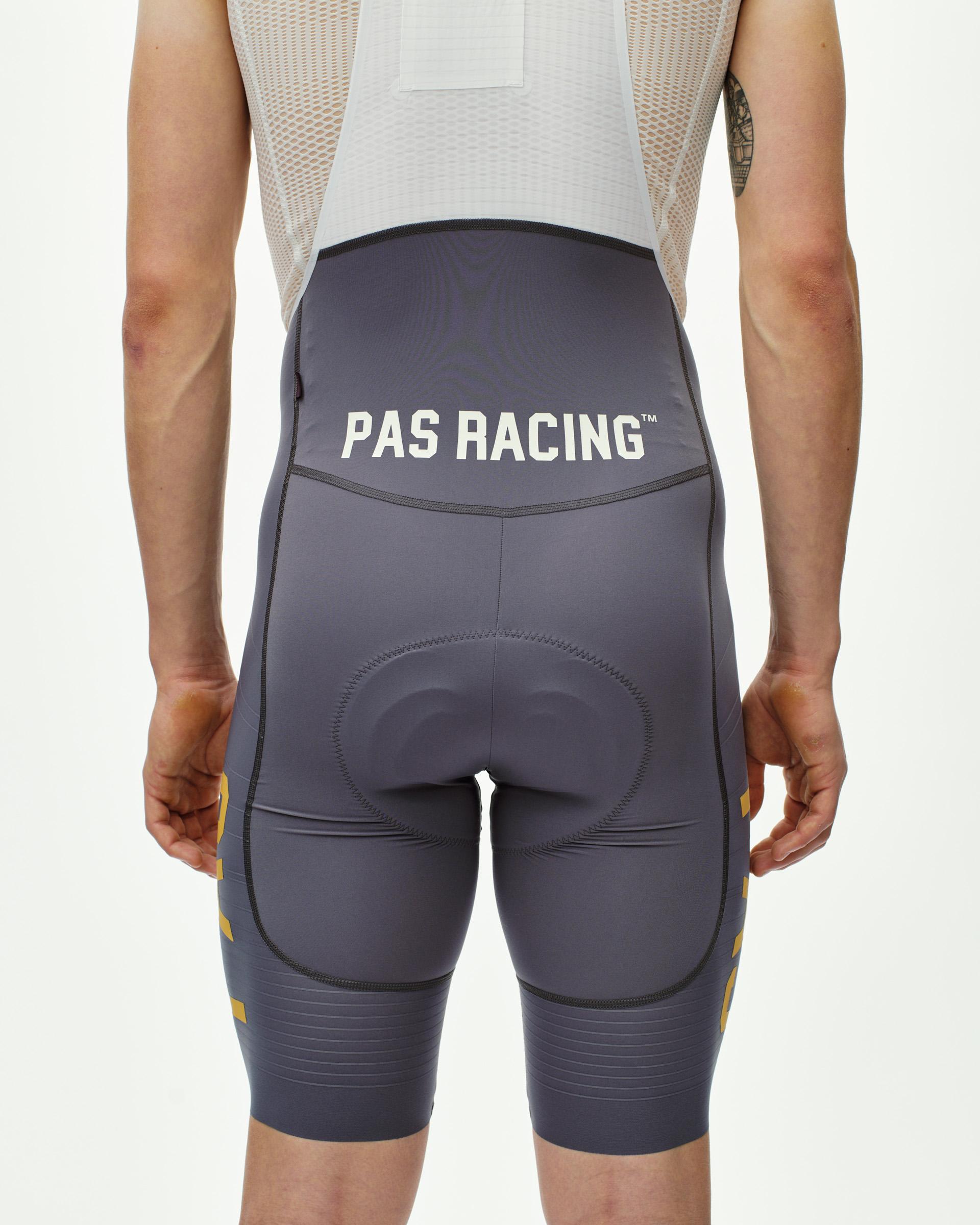 Grey Mechanism Pro Men's cycling bibs, rear view on model with PAS Racing waistband print and gold side stripes