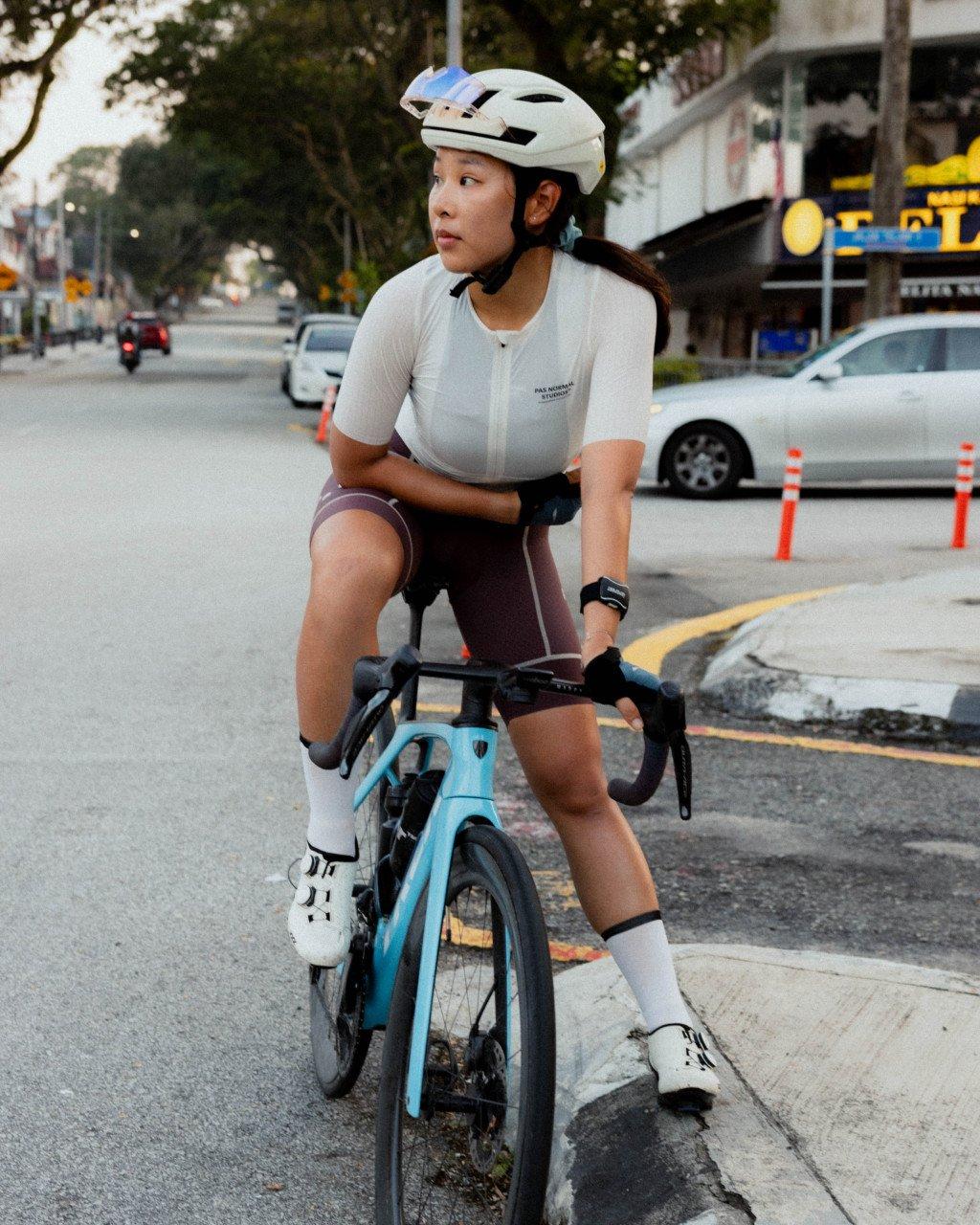 Model wearing white cycling jersey and burgundy shorts on time trial bike in urban Singapore street
