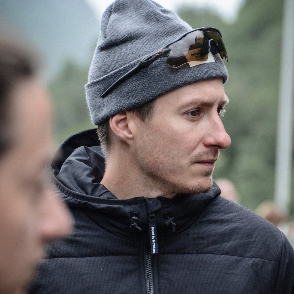 Model wearing grey beanie with sunglasses and dark hooded jacket outdoors