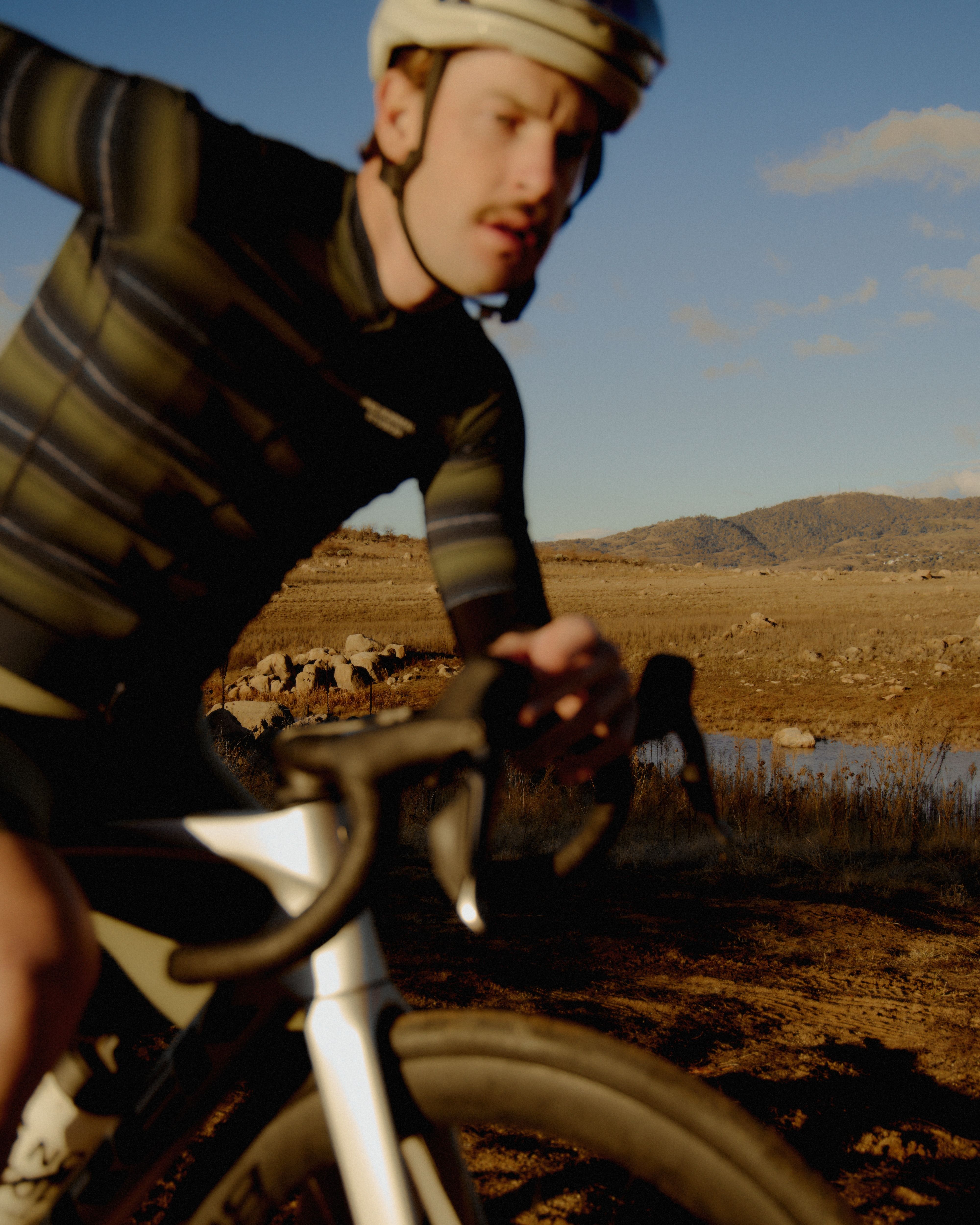 Model wearing dark cycling jersey with striped sleeves cycling through desert landscape