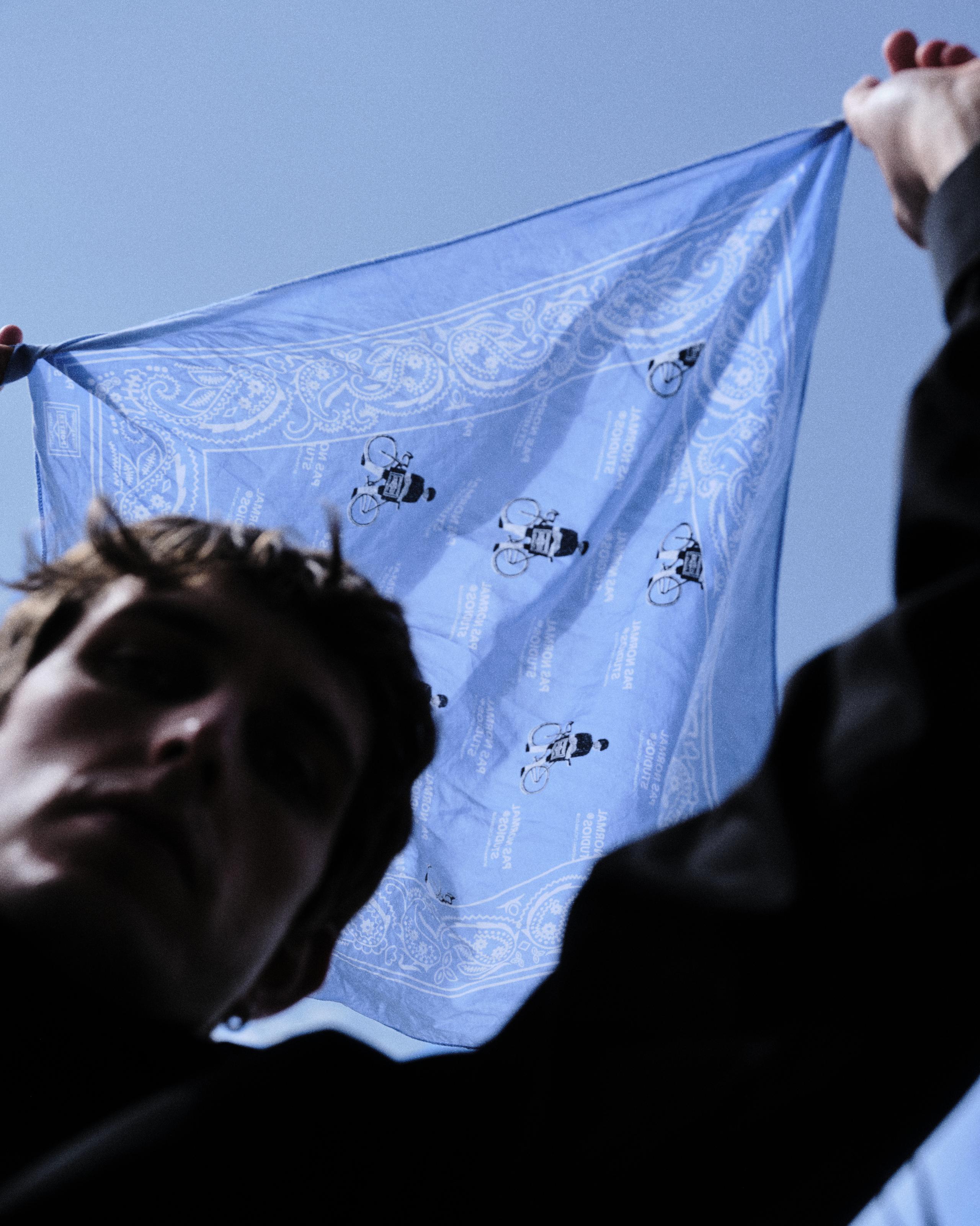 Model holding blue bandana with paisley pattern and cycling motifs against sky