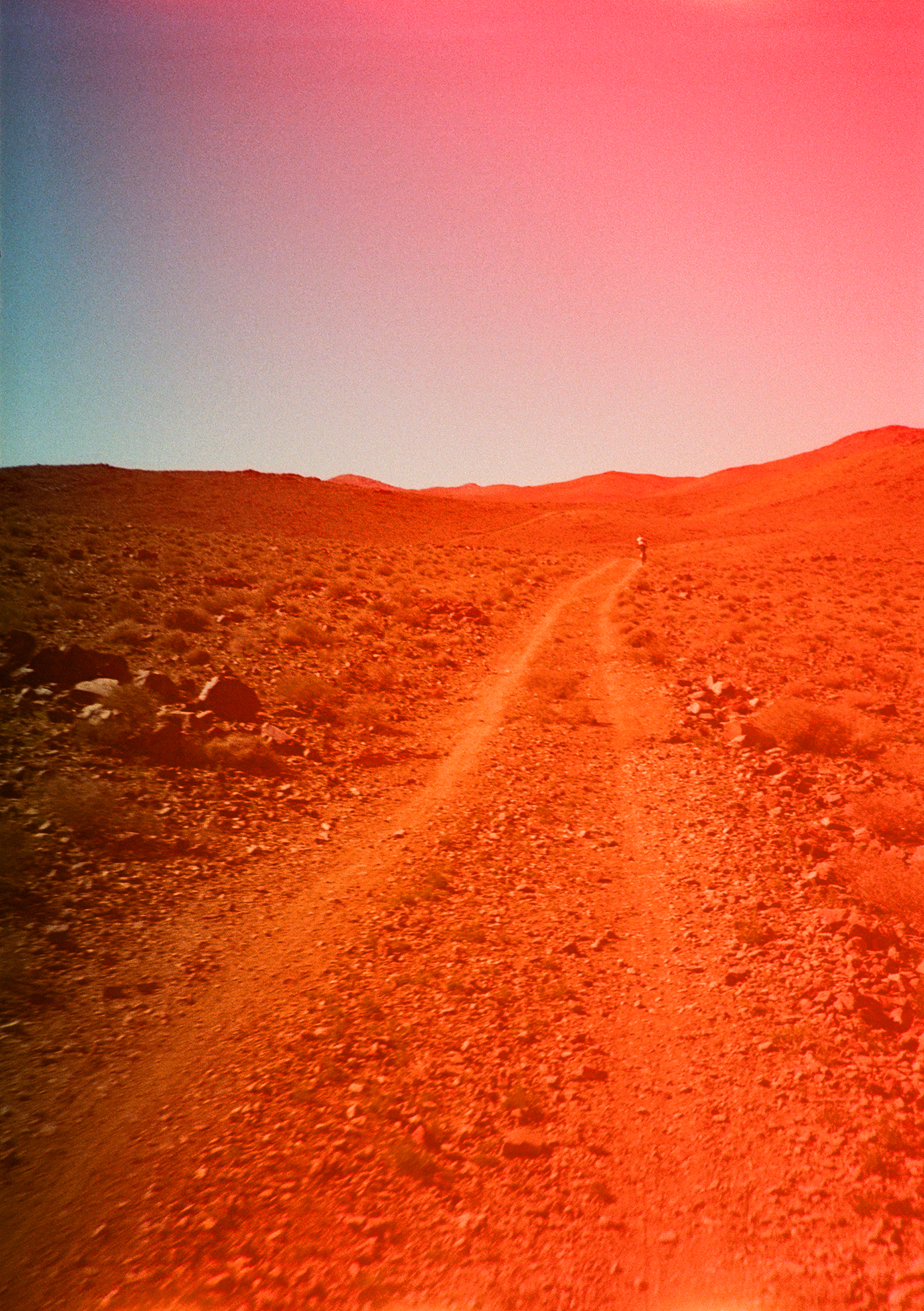 Cyclist on desert road through Atlas Mountains with orange-tinted landscape and gradient sky