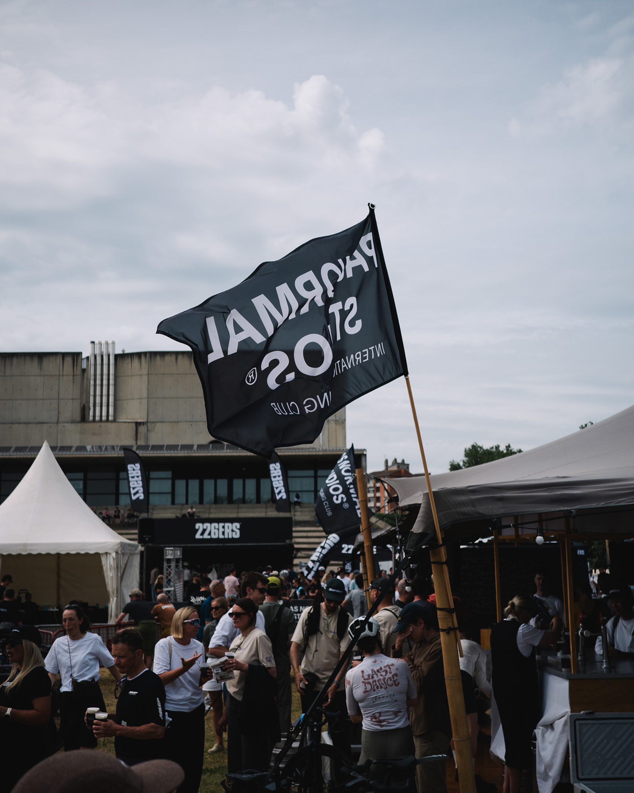 Black brand flag flying at cycling event with crowd and vendor tents