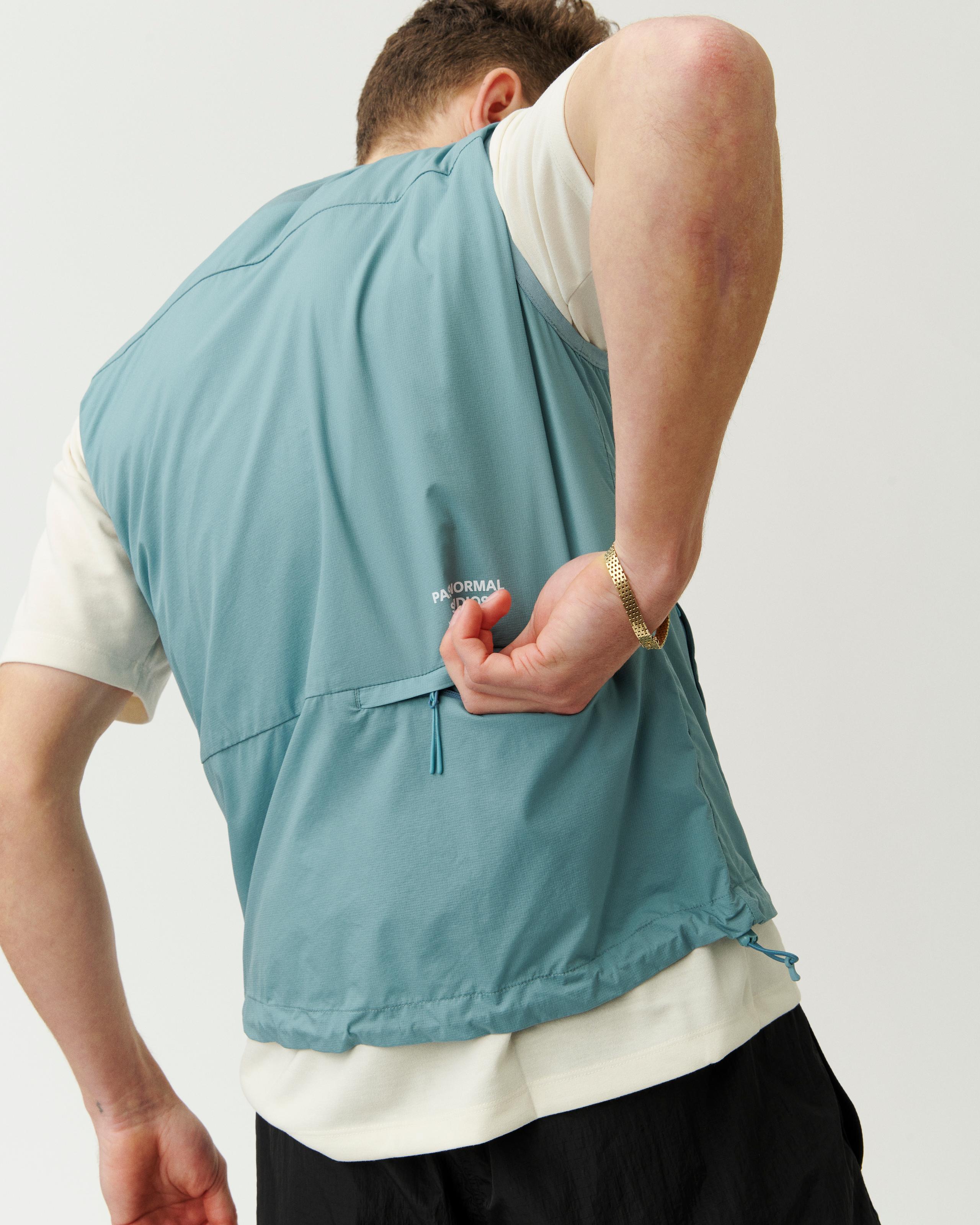 Dusty Blue Off-Race Stow Away vest on model, rear view showing zip back pocket and drawcord hem