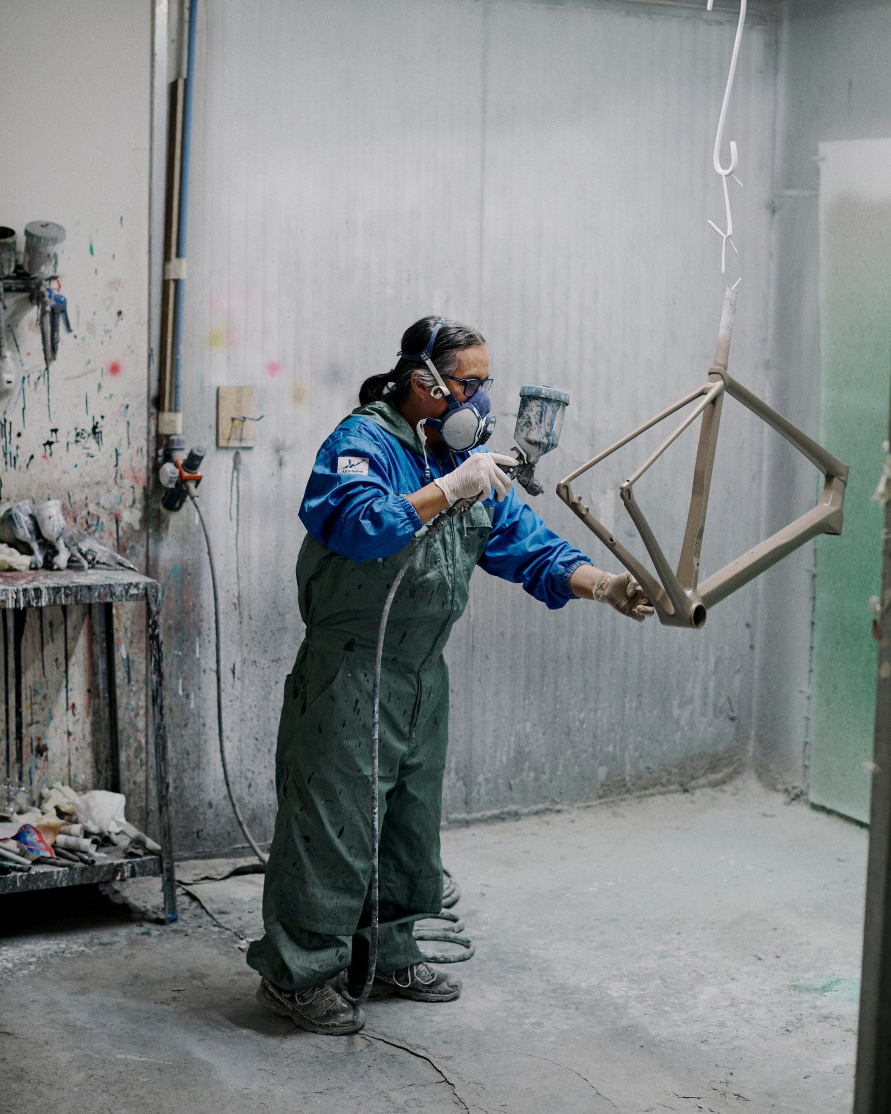 Craftsperson spray painting bicycle frame in workshop wearing protective gear and overalls