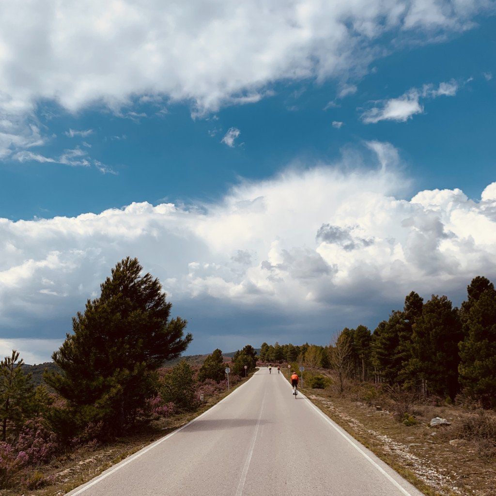 Cyclist on remote mountain road under dramatic cloudy sky with pine trees and Mediterranean landscape