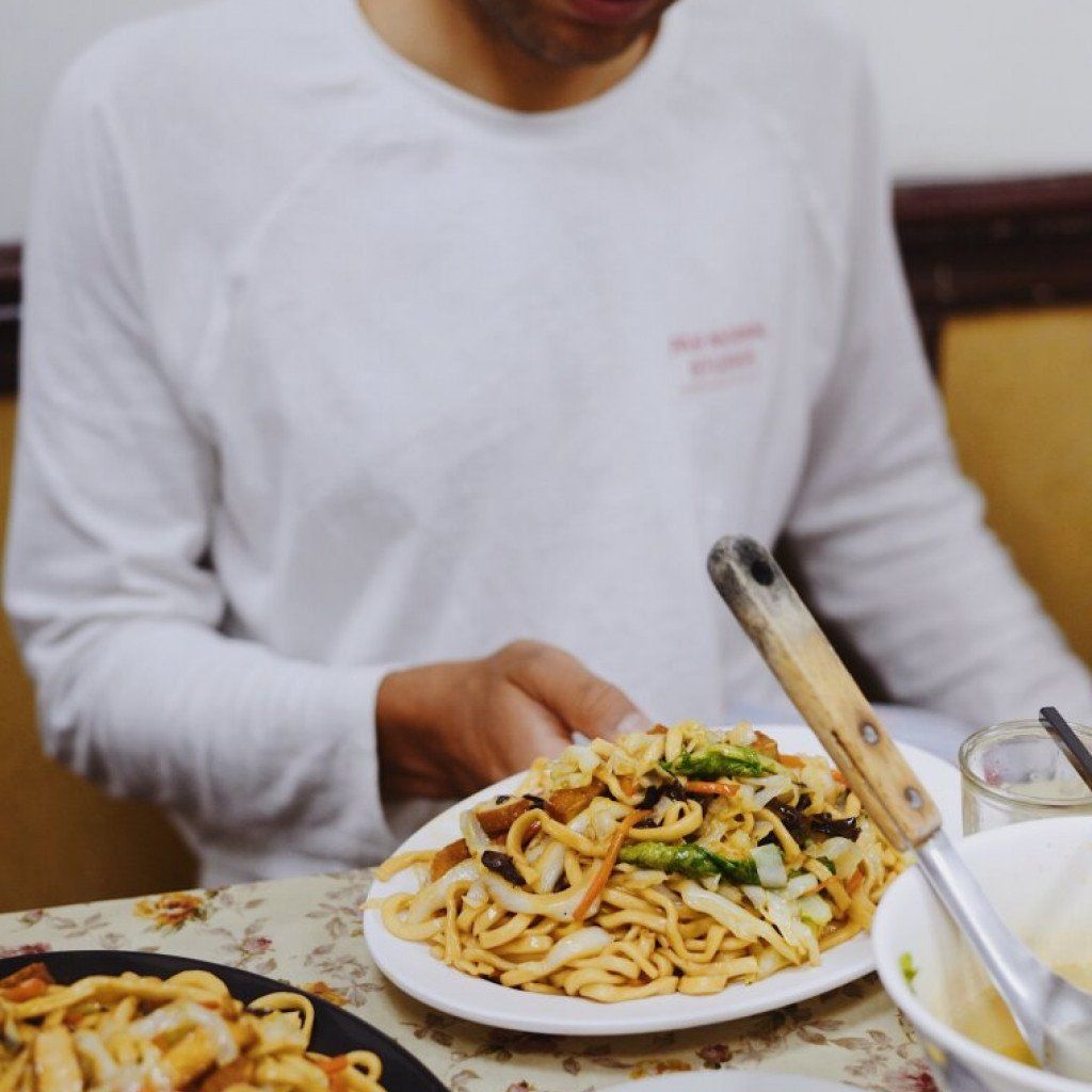 Model wearing white long-sleeve shirt with chest logo while eating noodles