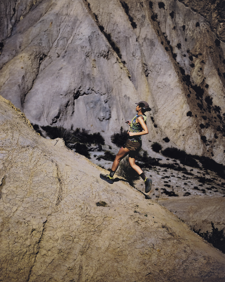 Model wearing camo pattern running gear while trail running on rocky desert terrain