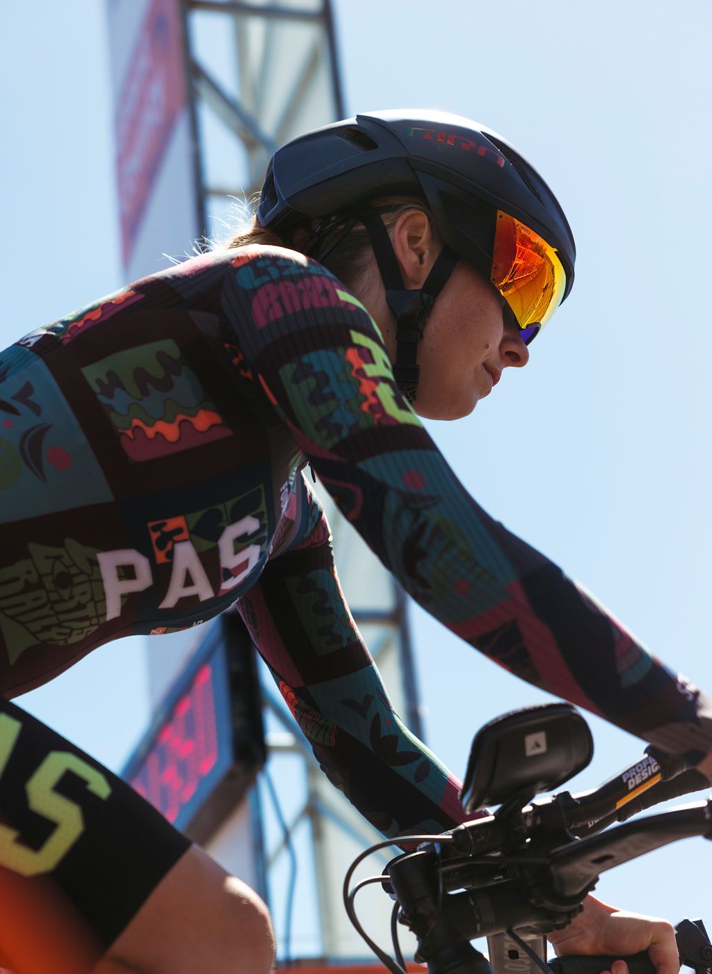 Model wearing PAS collection tri suit with colorful geometric pattern in racing position on time trial bike