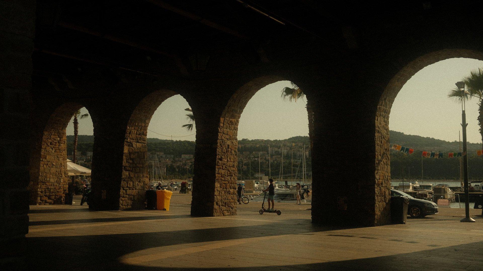 Stone arches framing Mediterranean harbor with boats and hills in background