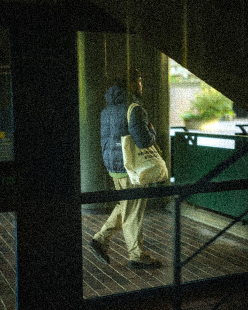 Model wearing blue quilted jacket and cream tote bag walking through urban underpass