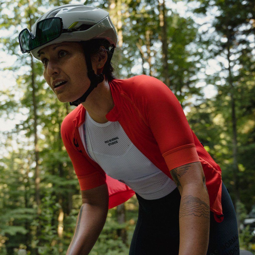 Model wearing red cycling jersey with white mesh panel and aero helmet in forest setting