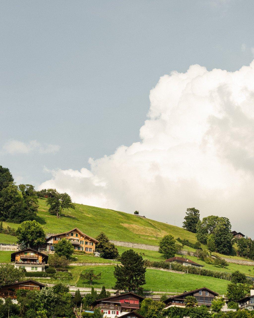 Alpine village with green rolling hills and traditional wooden houses under cloudy sky