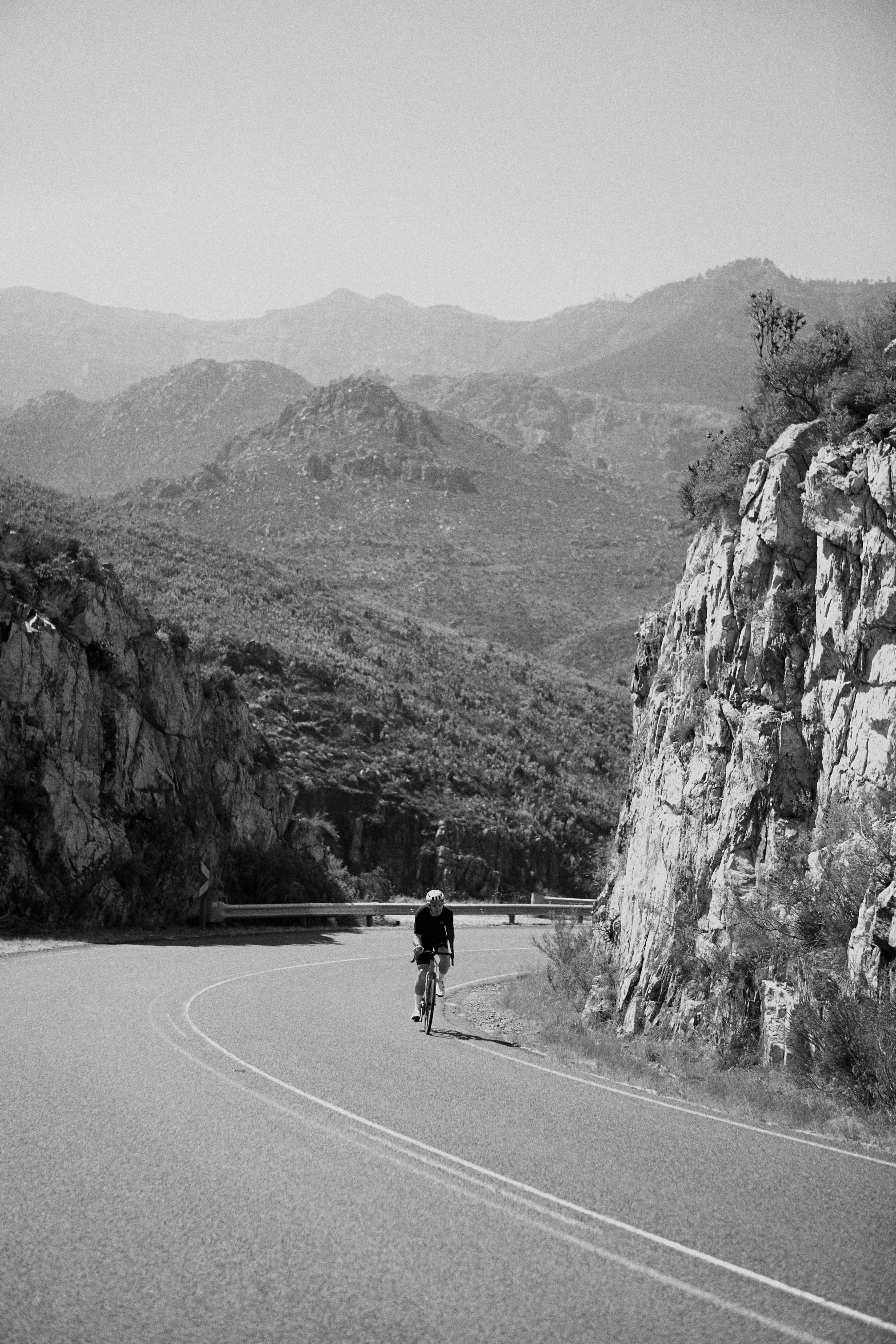 Cyclist on mountain road through rocky canyon landscape in black and white