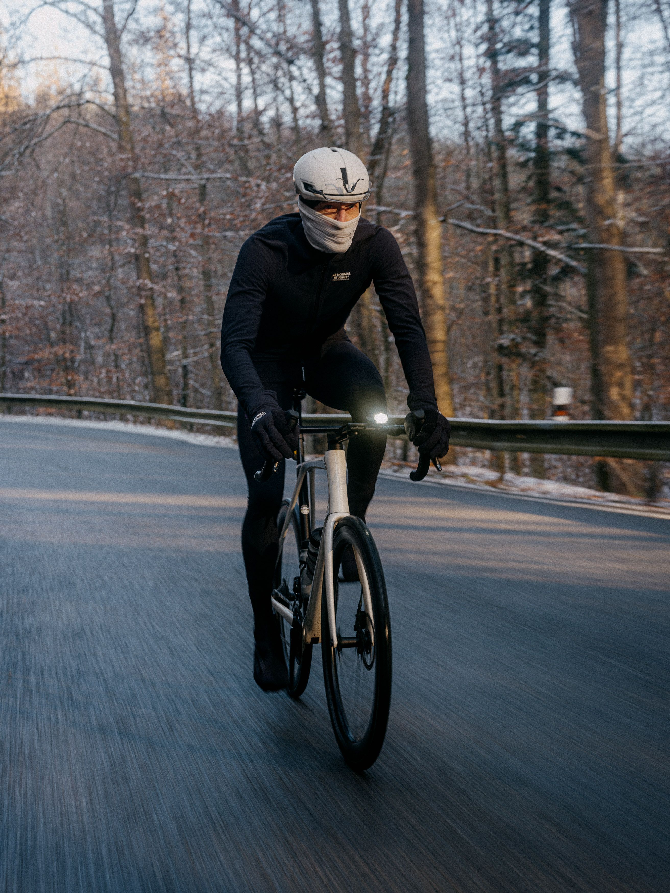 Model wearing black cycling apparel on time trial bike on winter road with face covering and helmet